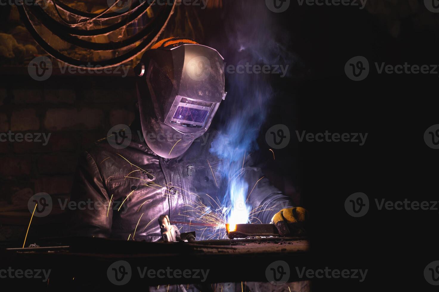 man in a welding mask welds a pipe in a dark workshop. welding smoke in the face, close-up photo