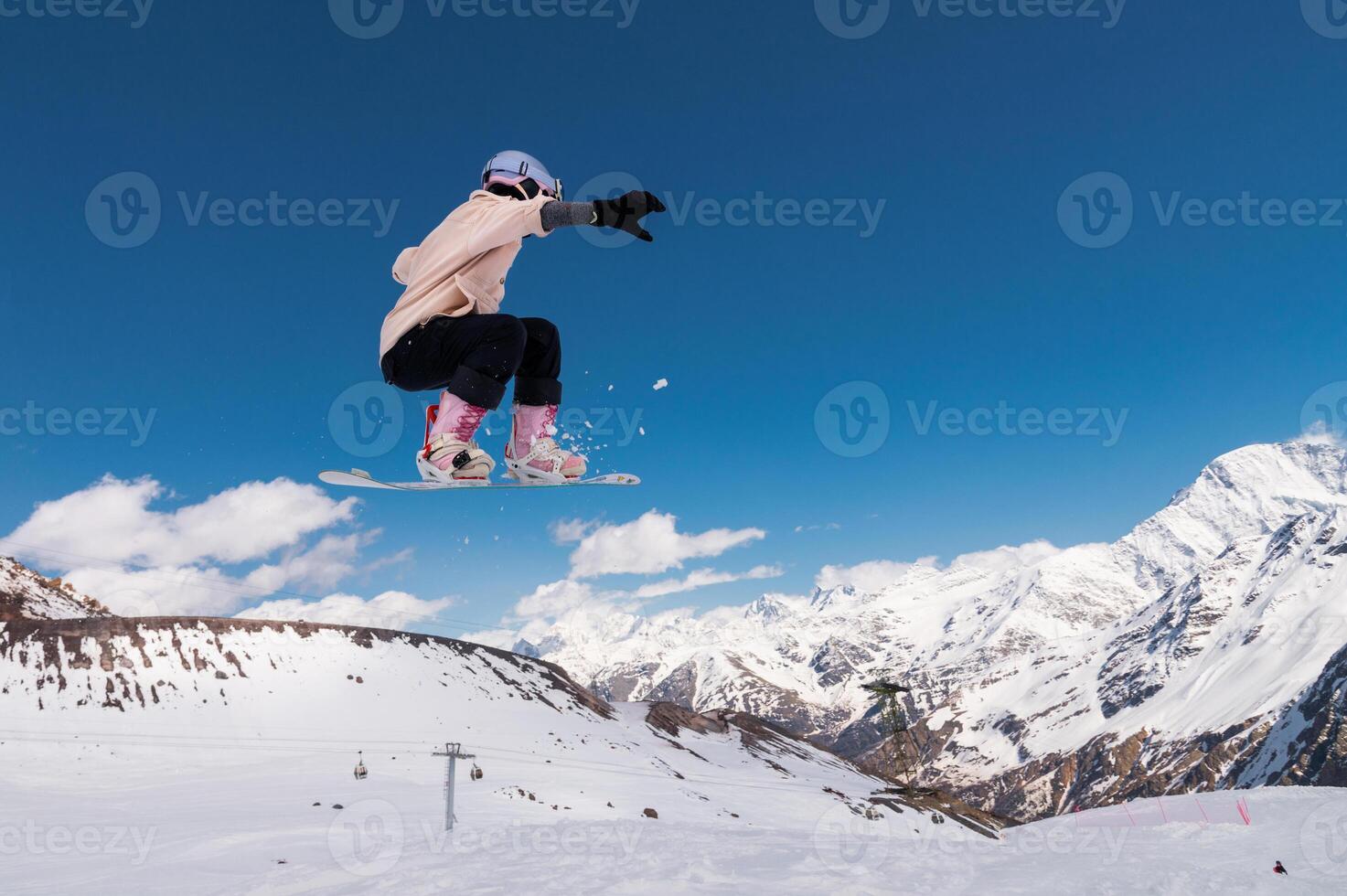 young woman snowboarder jumping from a springboard in the snowy mountains photo