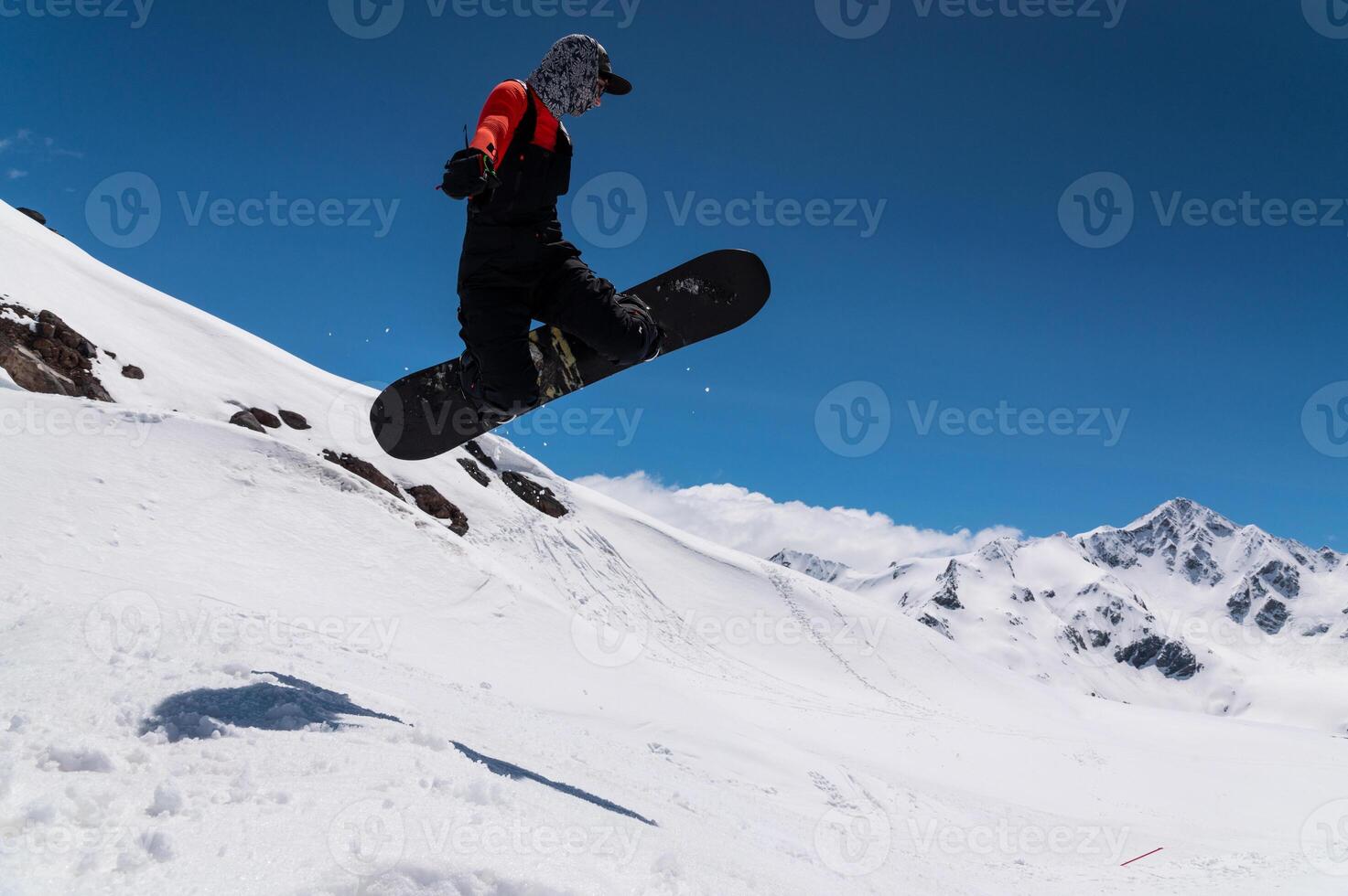 A woman snowboarder makes a ski jump against the backdrop of high snow-capped mountains photo