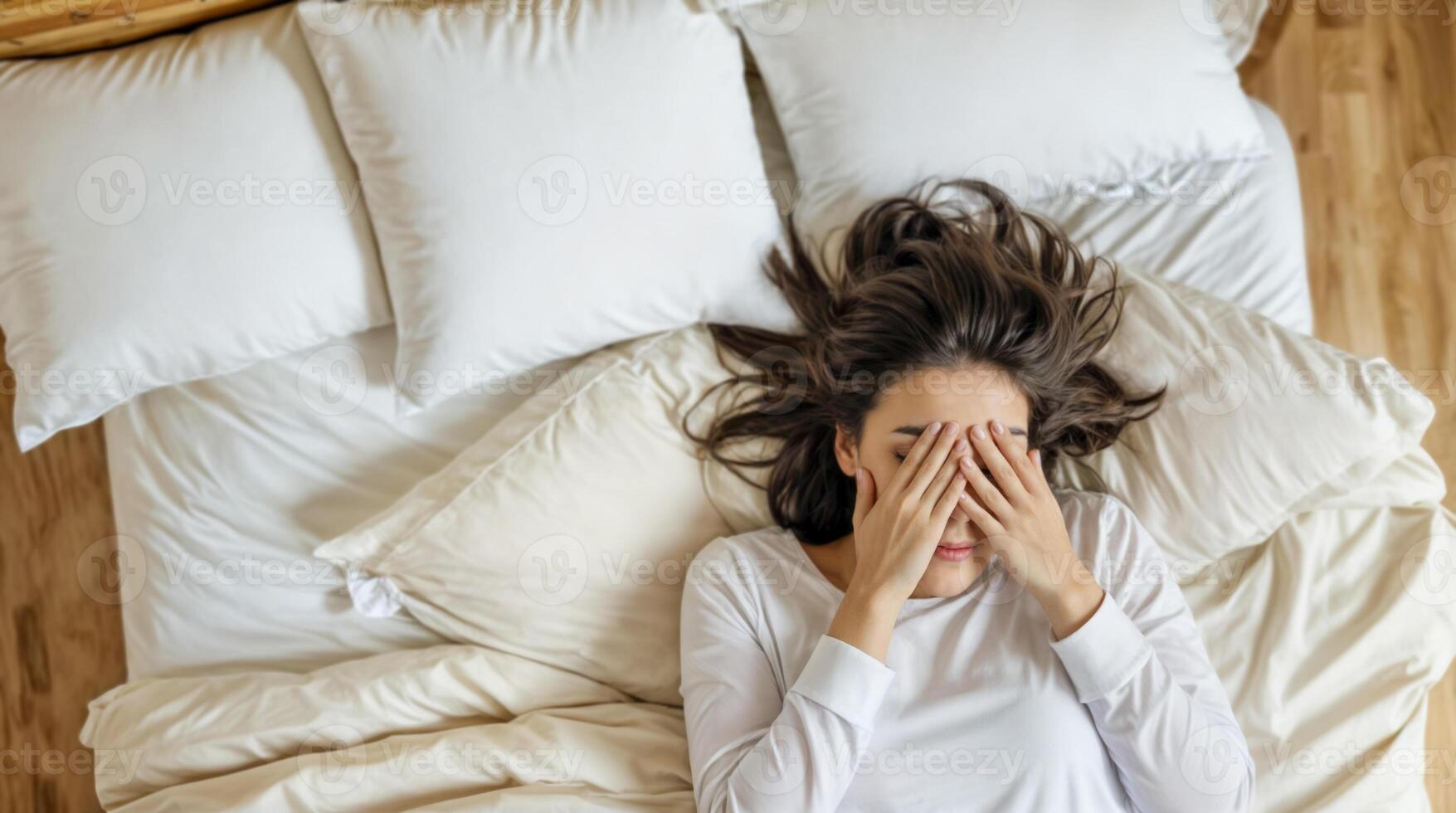 Young woman lying in bed with hands on face, feeling stressed photo