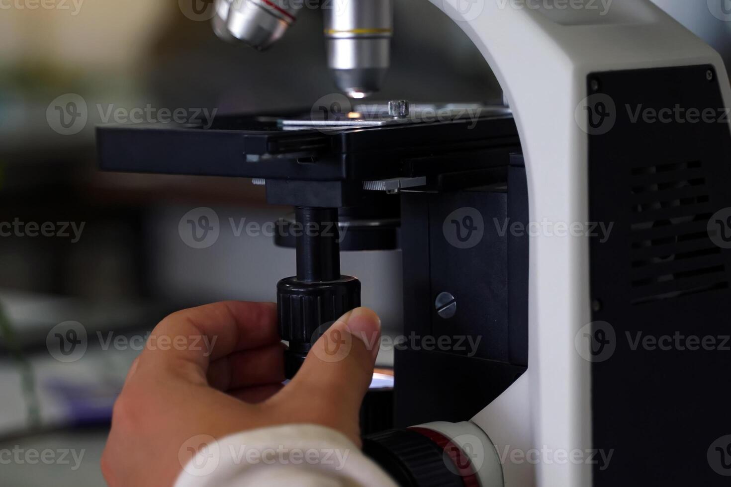 Hand turns the microscope's fine focus adjustment knob to increase the sharpness of the image. microscope is a piece of equipment in a science laboratory used to enlarge small images. photo