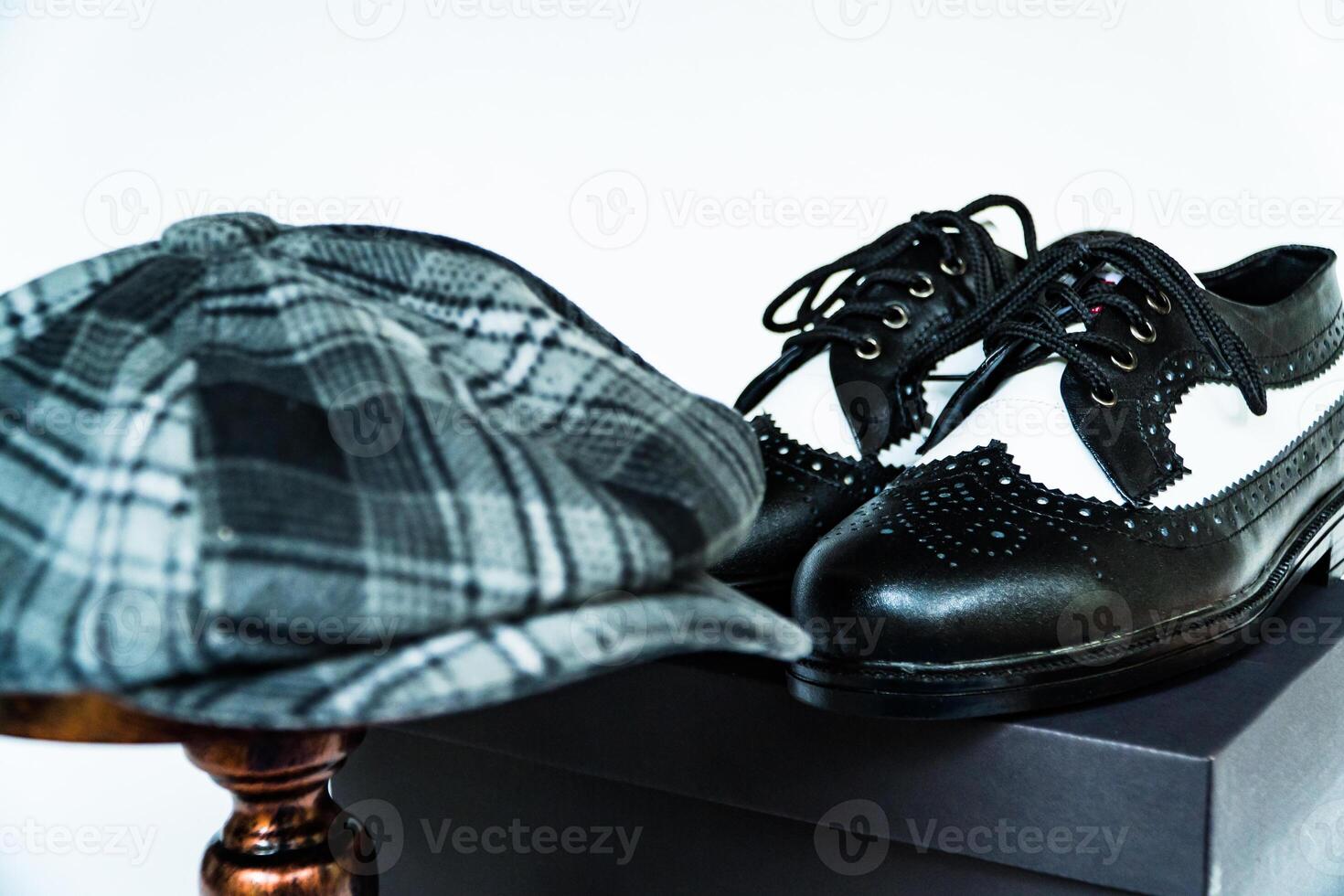 Classic studio photo concept of vintage two-tone wingtip shoes in genuine leather with newsboy cap or scaly hat on bronze mannequin on isolated white background