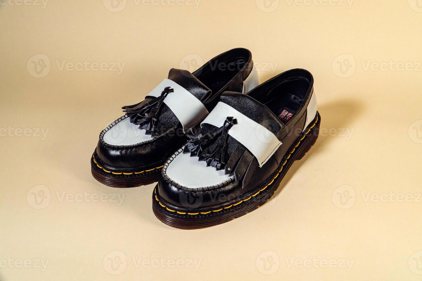 Isolated photo of an elegant and shiny two-tone vintage shoe product on a beige background. Close up of black and white tassel shoes with rubber outsole made from genuine cowhide.