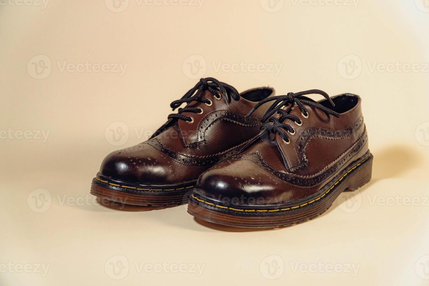 Close-up of dark brown gradient wingtip shoes with rubber outsole made of genuine cowhide. Concept studio photo of an elegant and shiny vintage shoe product on a beige background