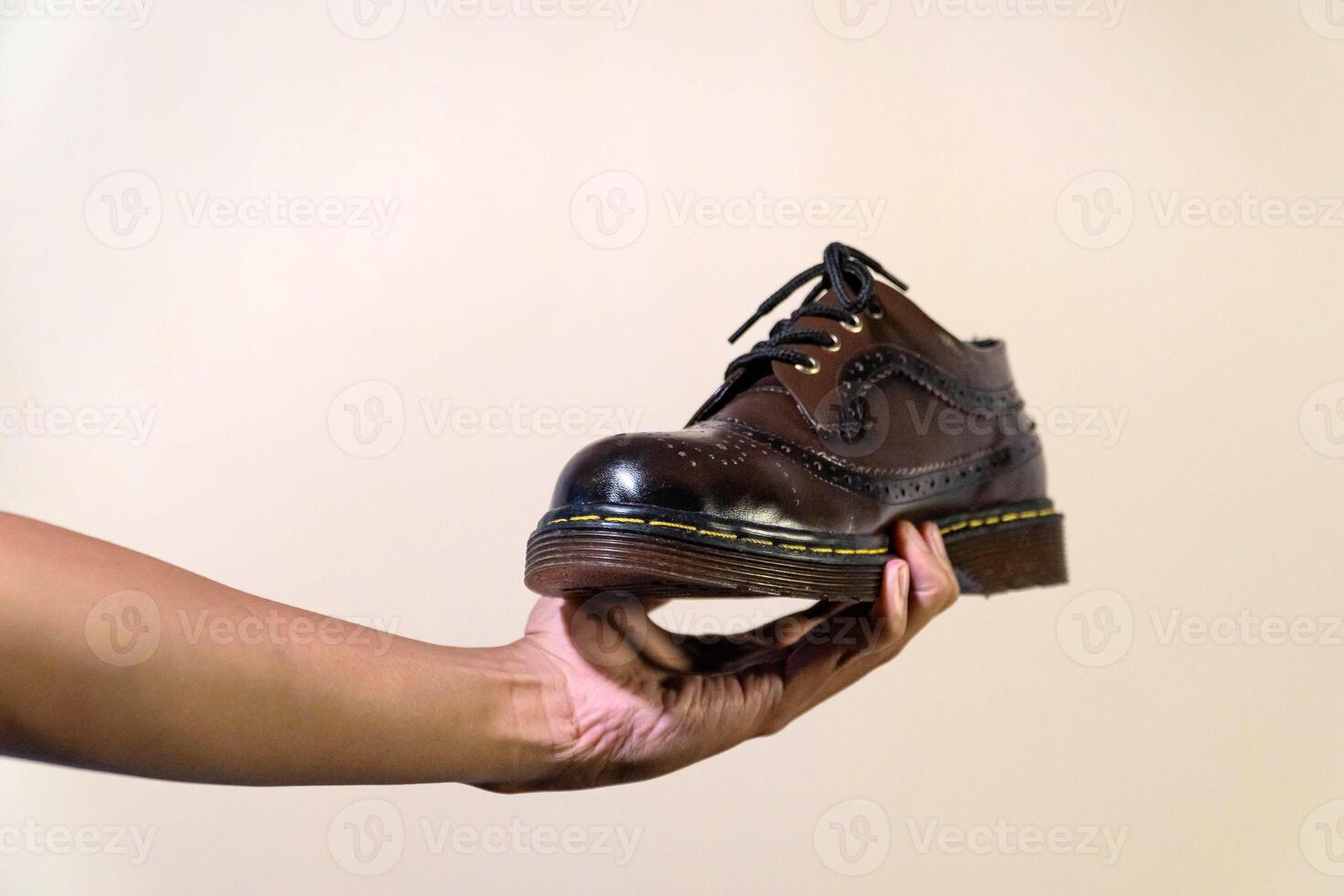 Men's hands holding elegant and shiny vintage shoes on a beige background. Wingtip shoes are dark brown and elegant with a rubber outsole photo
