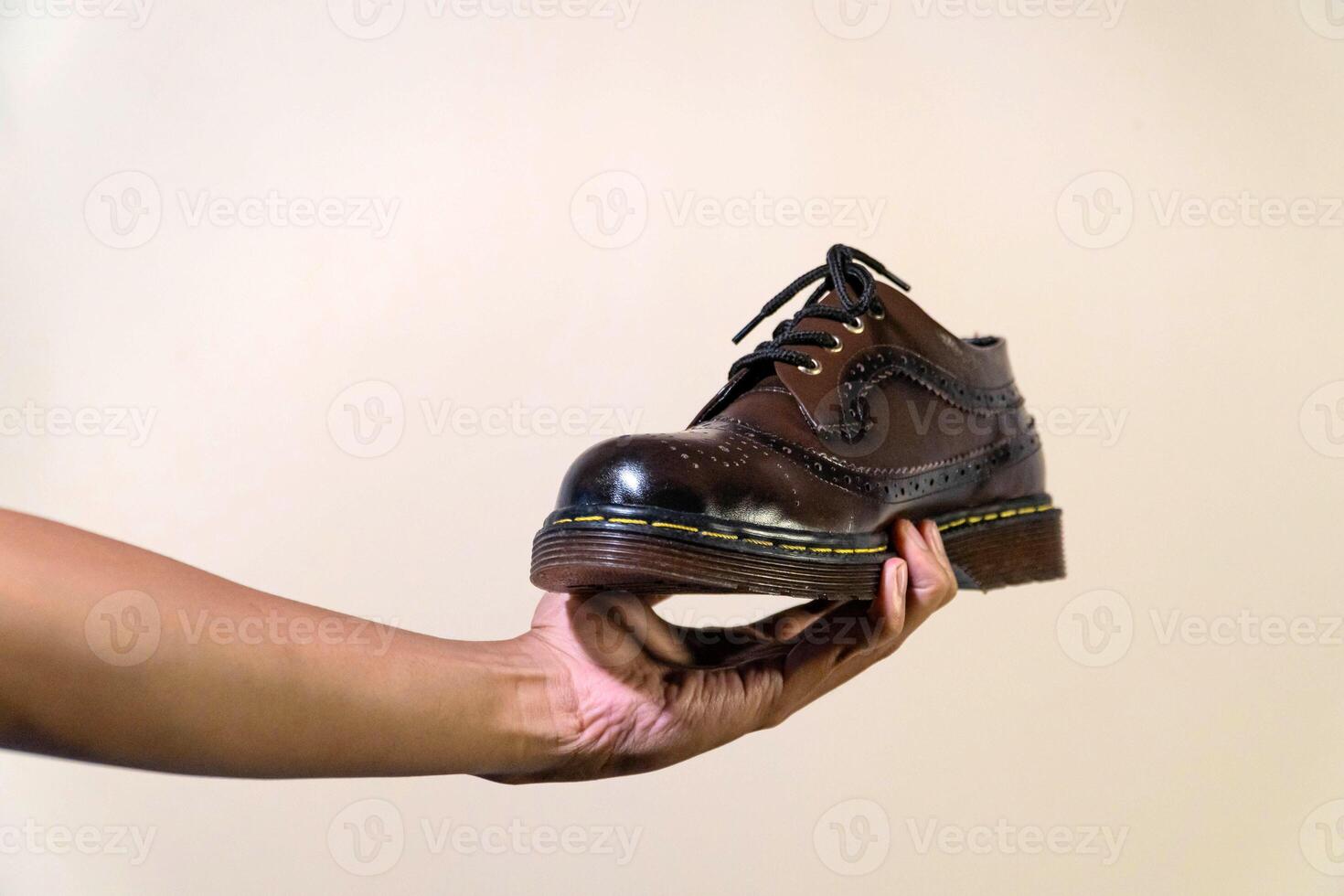 Men's hands holding elegant and shiny vintage shoes on a beige background. Wingtip shoes are dark brown and elegant with a rubber outsole photo