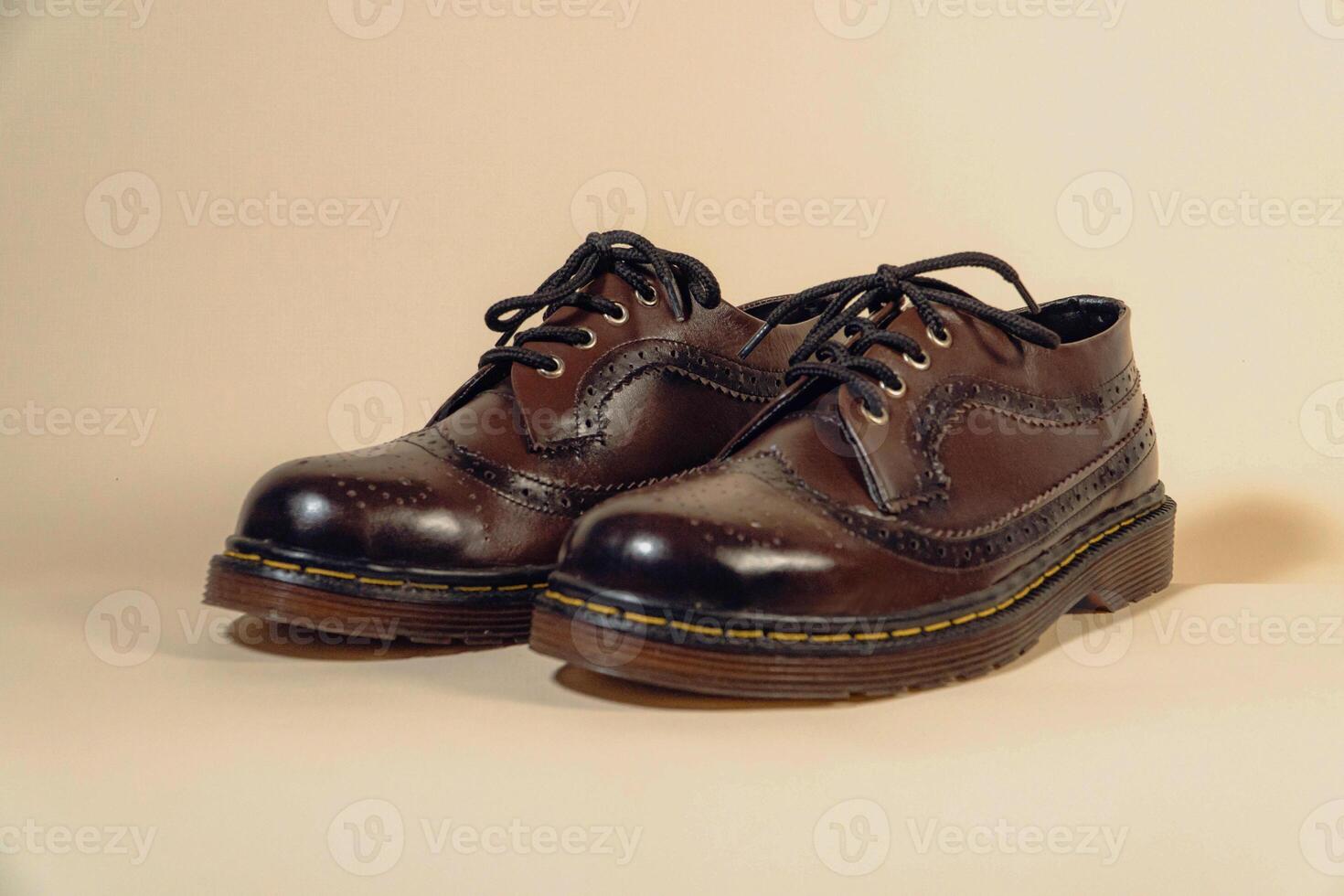 Close-up of dark brown gradient wingtip shoes with rubber outsole made of genuine cowhide. Concept studio photo of an elegant and shiny vintage shoe product on a beige background