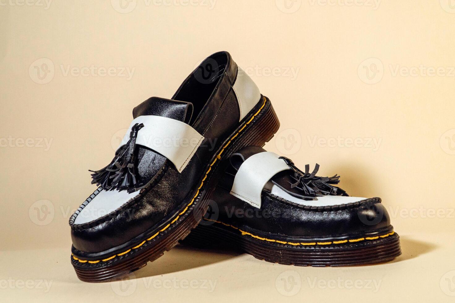 Isolated photo of an elegant and shiny two-tone vintage shoe product on a beige background. Close up of black and white tassel shoes with rubber outsole made from genuine cowhide.