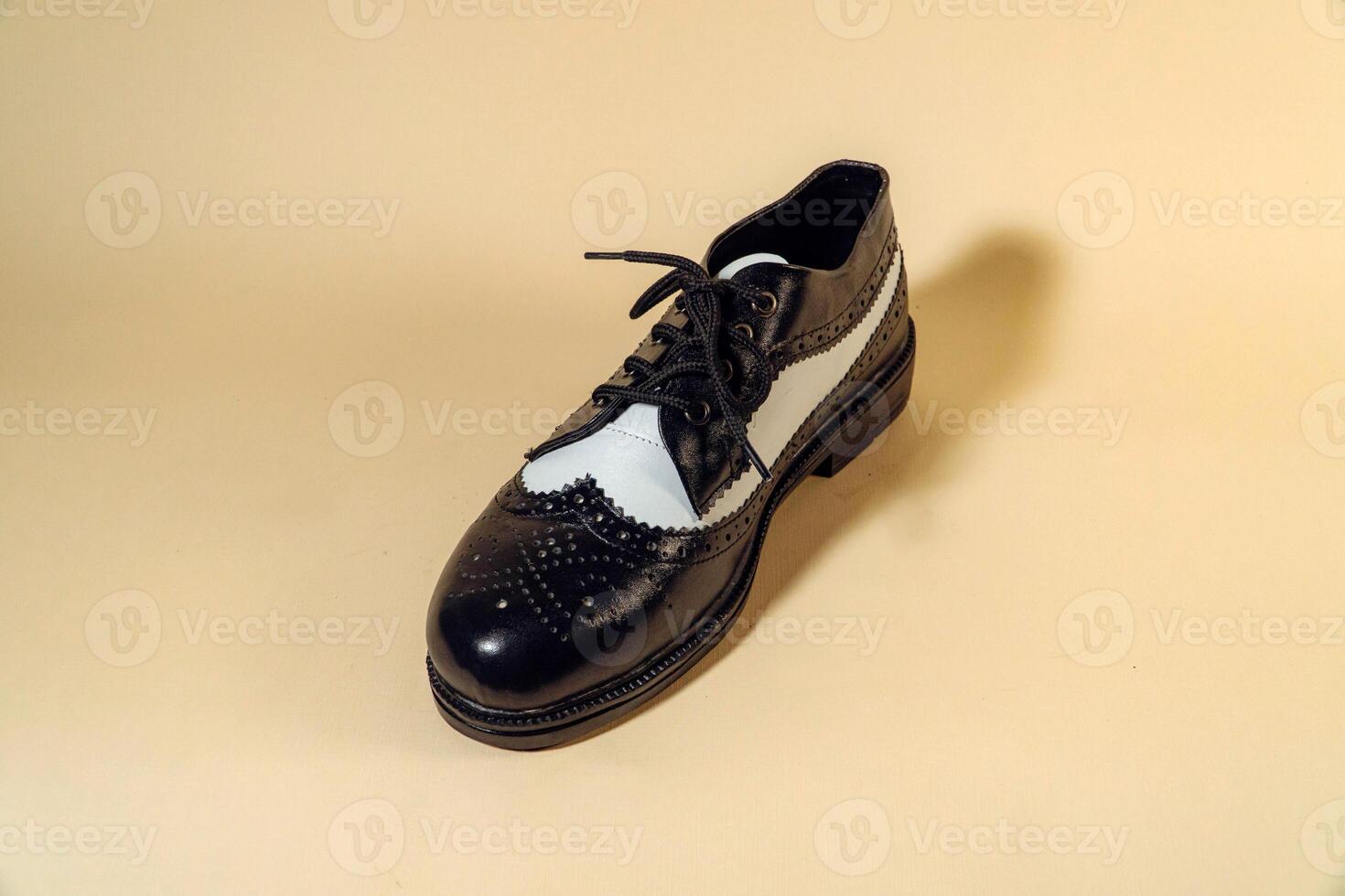 Close up of black and white brogue wingtip shoes with rubber outsole made of genuine cowhide. Studio shot of an elegant and shiny vintage two tone shoe product on a beige background photo
