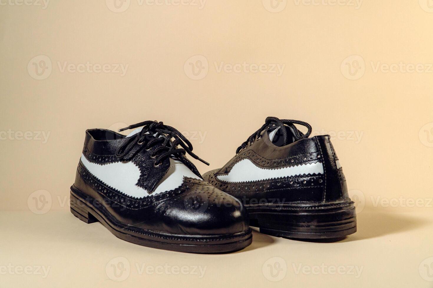 Close up of black and white brogue wingtip shoes with rubber outsole made of genuine cowhide. Studio shot of an elegant and shiny vintage two tone shoe product on a beige background photo