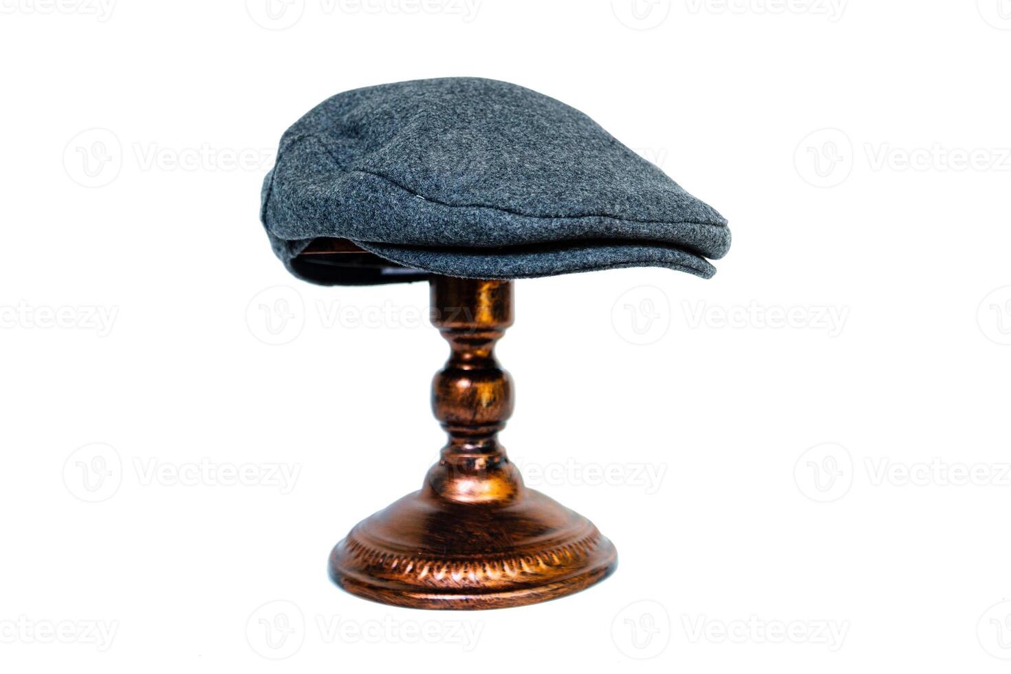 Detail of a scaly hat or flat cap or made of tweed herringbone mounted on a bronze mannequin head on a white background. Catalog photo of a classic dark gray hat on an elegant bronze mannequin
