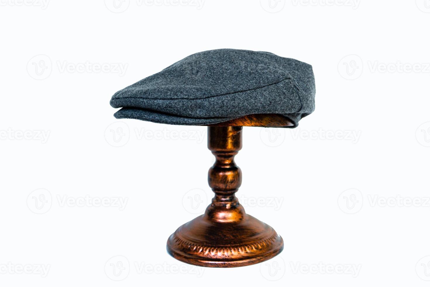 Detail of a scaly hat or flat cap or made of tweed herringbone mounted on a bronze mannequin head on a white background. Catalog photo of a classic dark gray hat on an elegant bronze mannequin