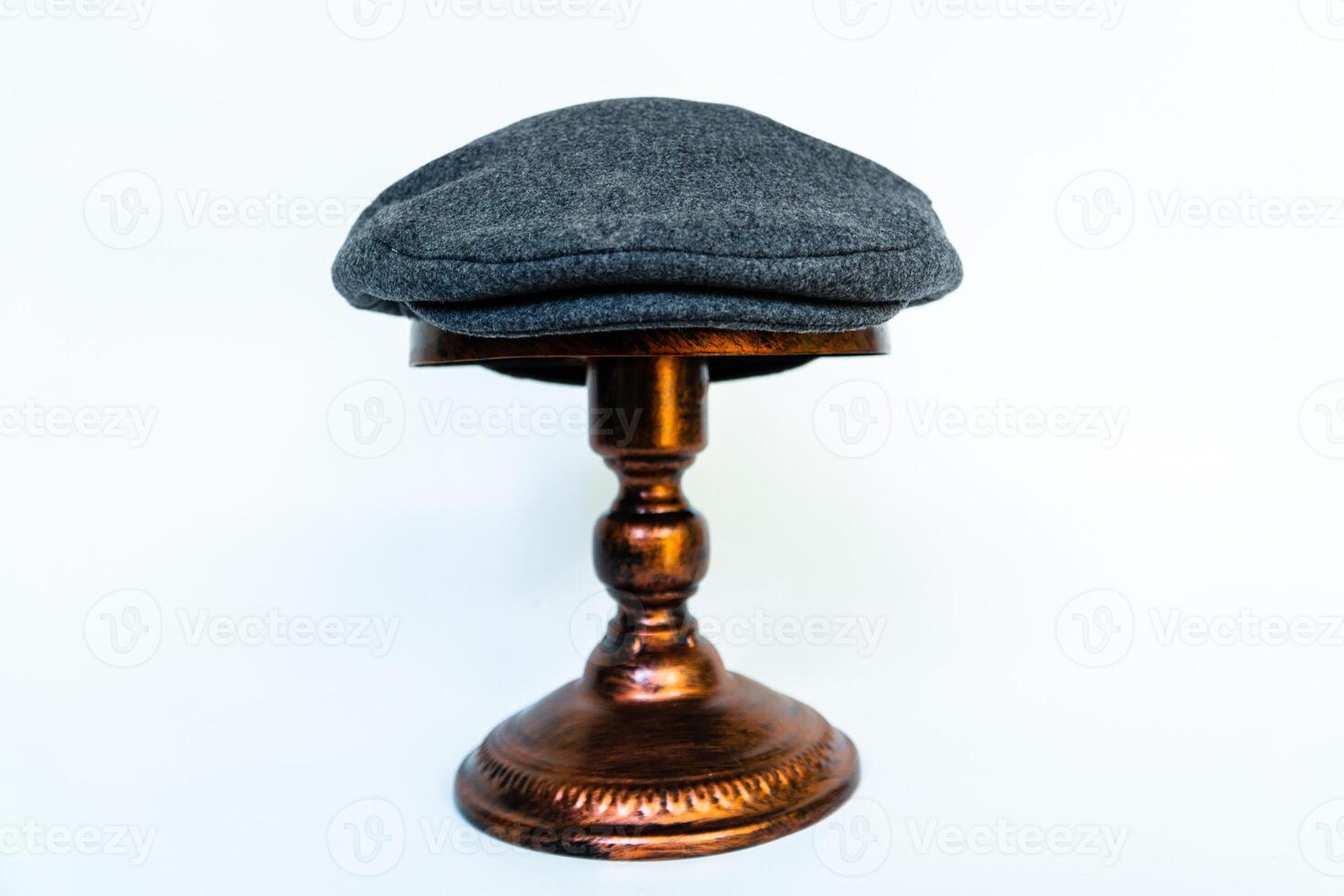 Detail of a scaly hat or flat cap or made of tweed herringbone mounted on a bronze mannequin head on a white background. Catalog photo of a classic dark gray hat on an elegant bronze mannequin