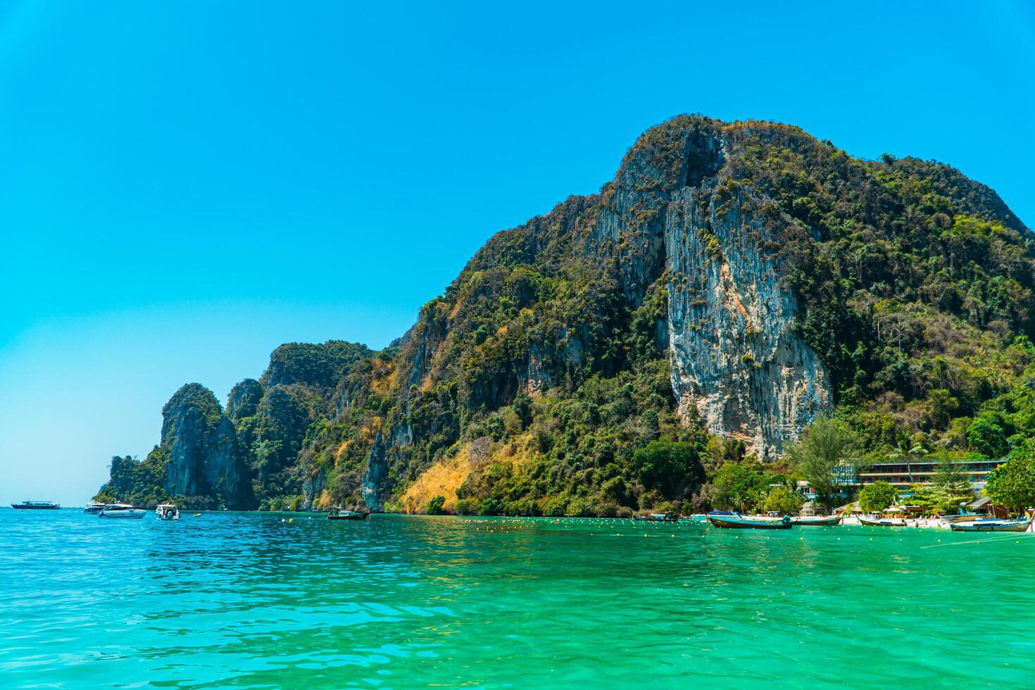 Large rock cliff covered in green trees with the sea in front of it on a sunny day. The view of large rock cliffs and vast ocean is a tourist icon for tropical islands in Krabi, Thailand photo