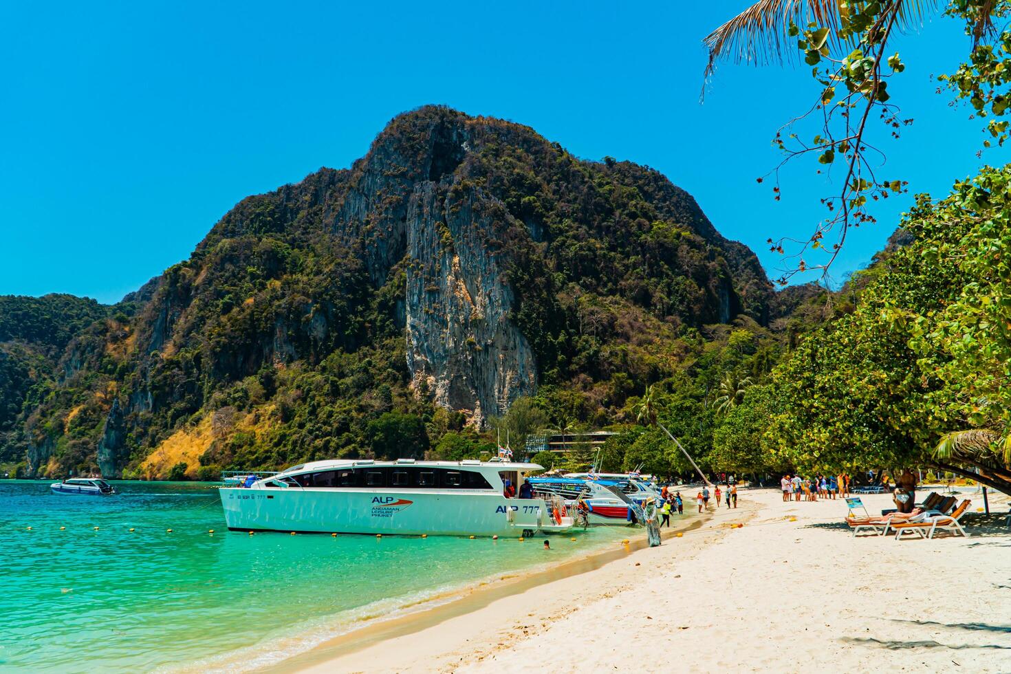 Large rock cliff covered in green trees with the sea in front of it on a sunny day. The view of large rock cliffs and vast ocean is a tourist icon for tropical islands in Krabi, Thailand photo