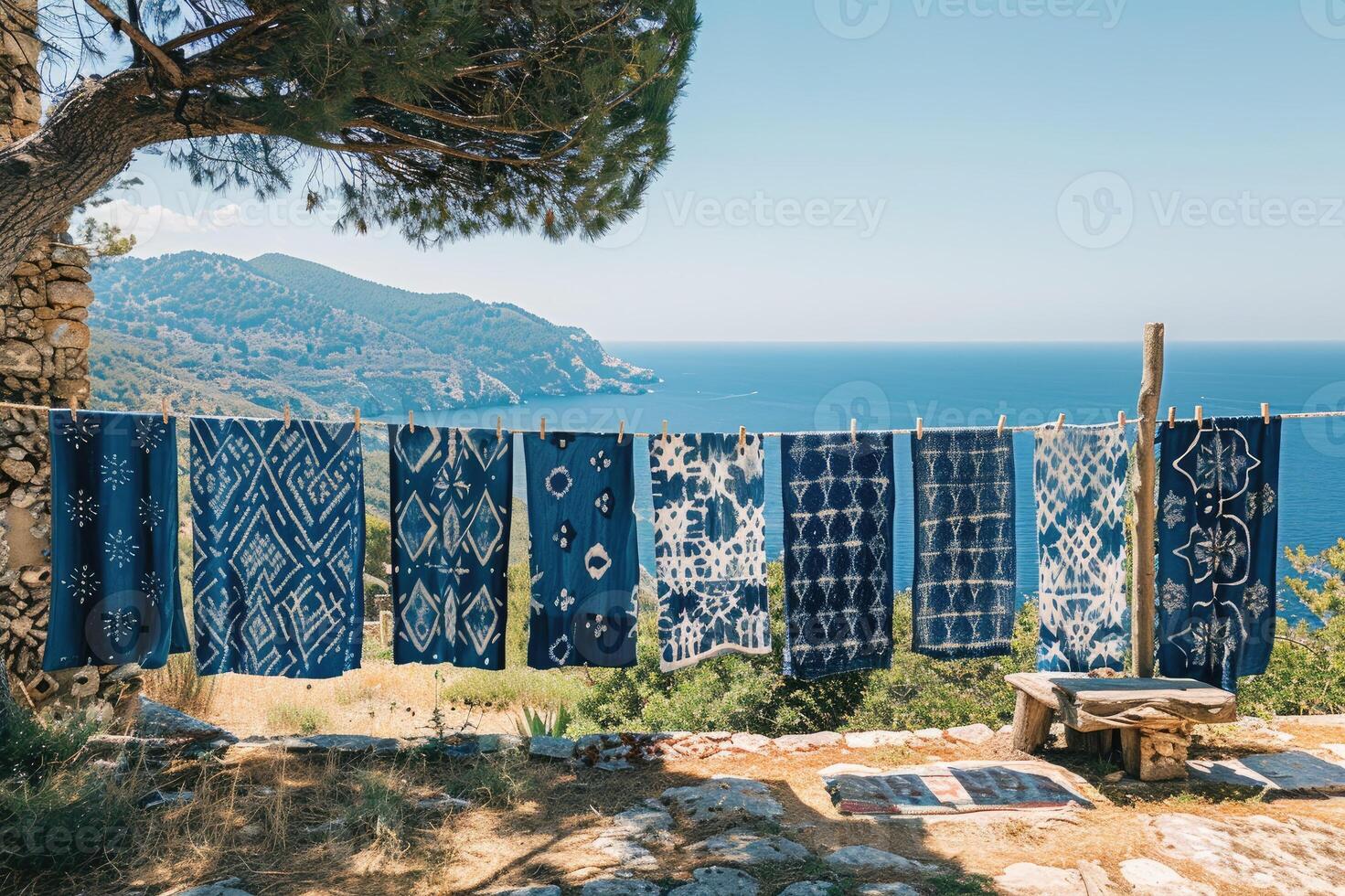 Beautifully patterned blue fabrics hanging on a clothesline under a tree, set against a peaceful mountain backdrop near the sea. photo