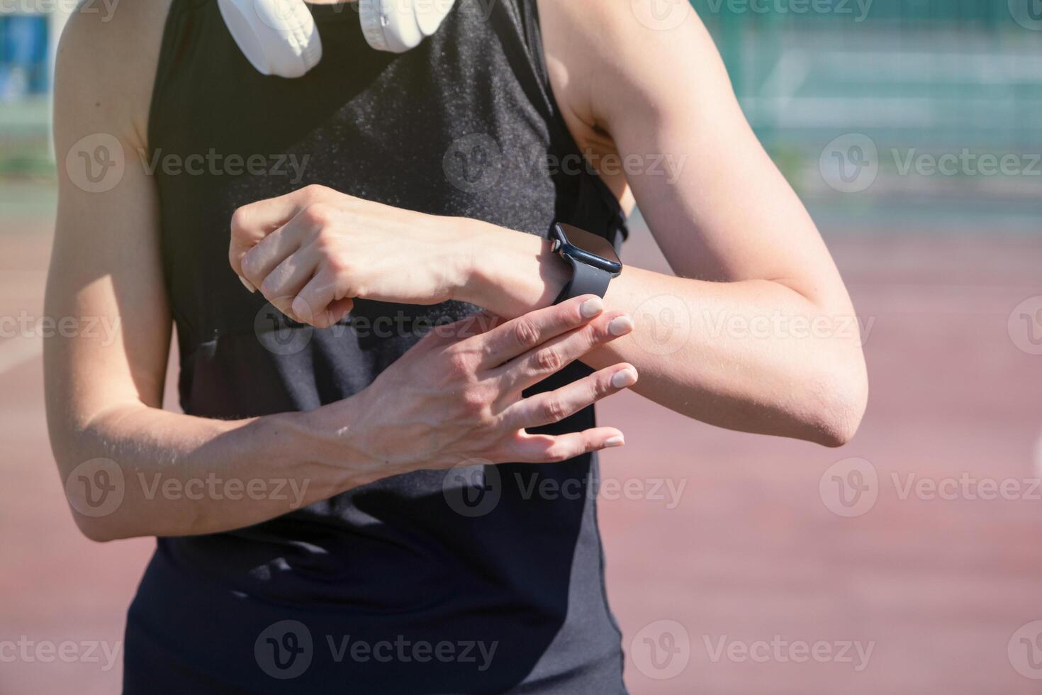 woman exercising in the stadium, checking mobile app on his wristwatch, taking pulse or heart rate after heavy workout outdoor photo