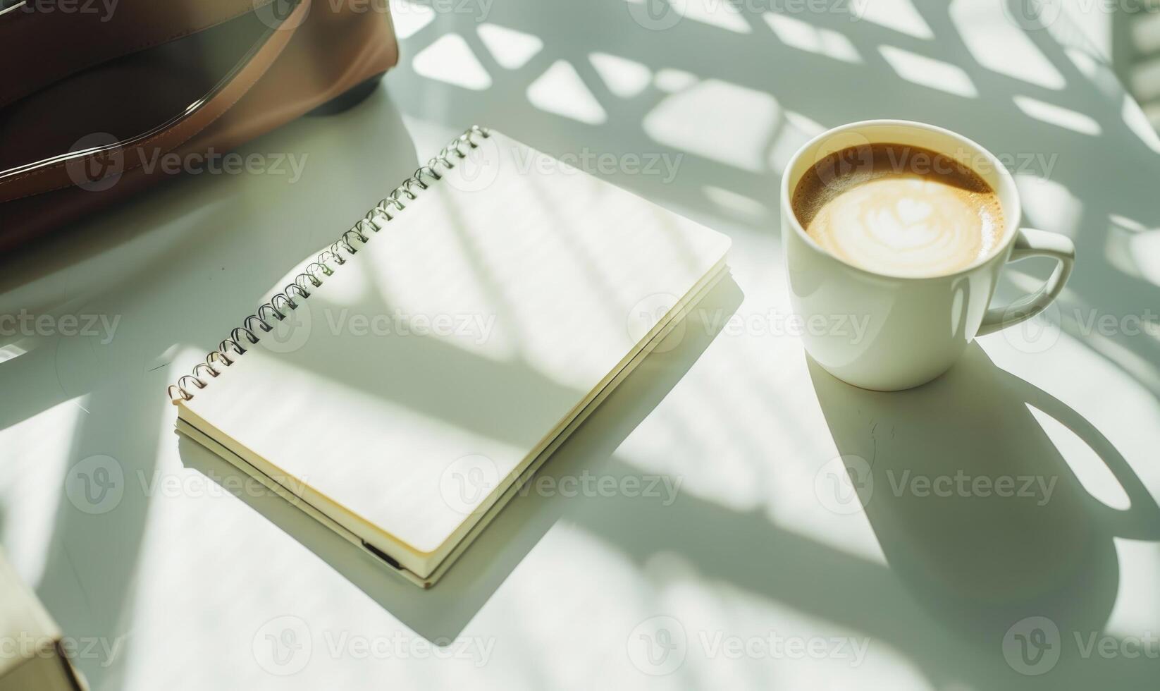 Closed notebook on a white table with a cup of coffee and a handbag photo