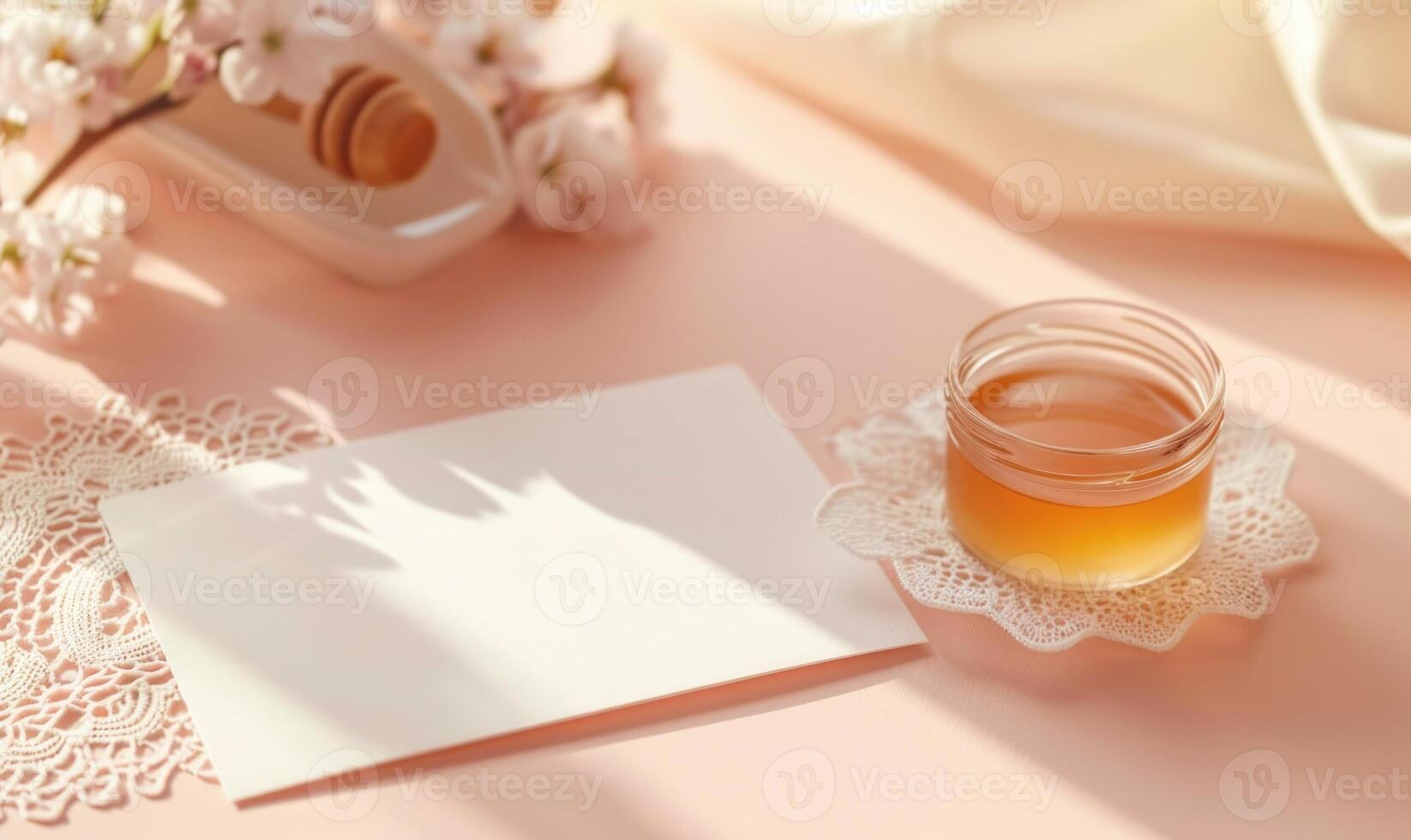 White blank card on a pastel peach table, with a delicate lace doily and a small glass jar of honey photo