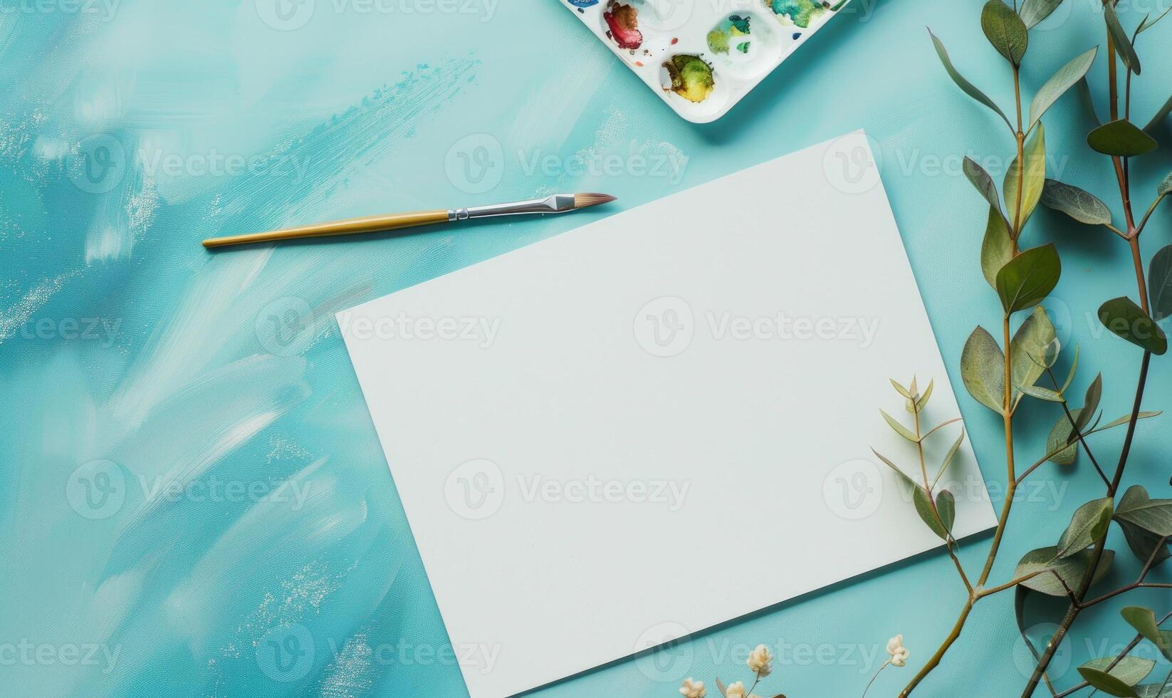 White blank card on a pastel turquoise background, with a small watercolor palette and brushes photo