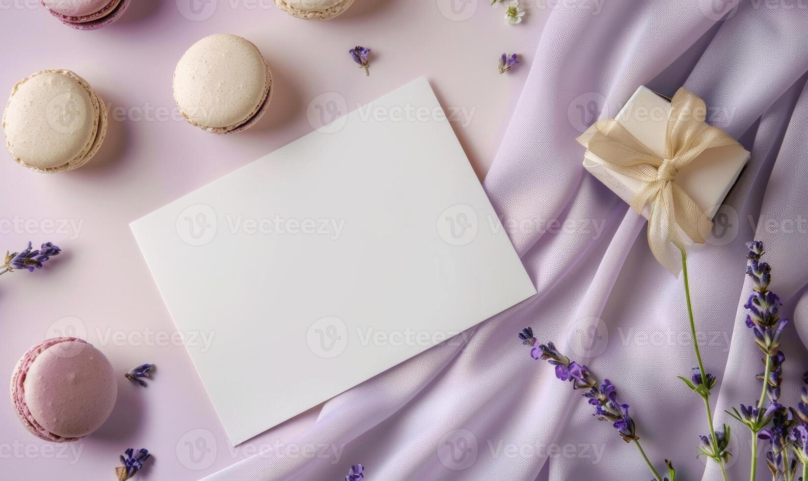 White blank card on a pastel lilac table, with a silk ribbon and a small box of macarons photo