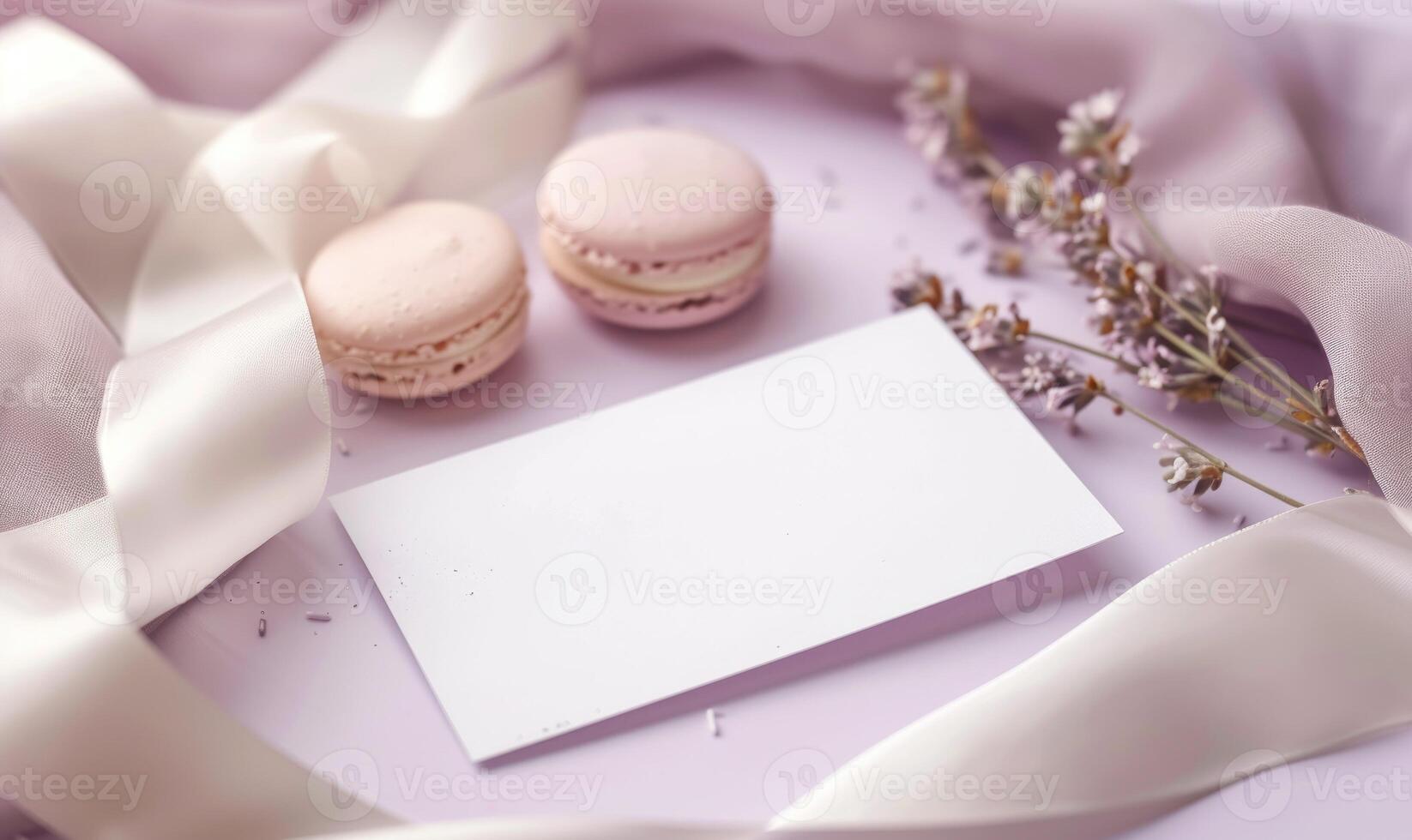 White blank card on a pastel lilac table, with a silk ribbon and a small box of macarons photo