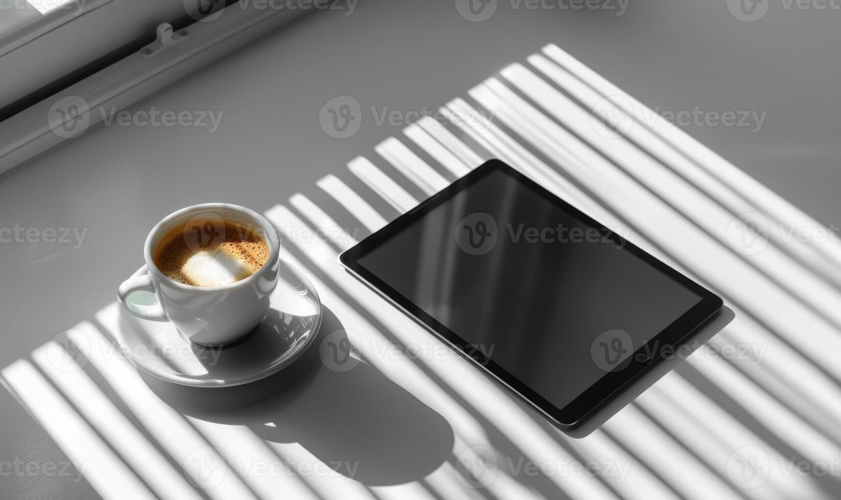 Tablet on a light gray table with a cup of tea on the left, sunlight from window photo