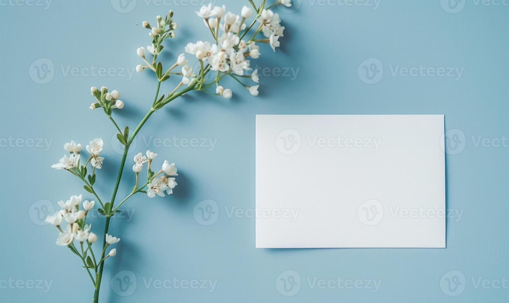 White blank card on a pastel blue background, with a small bouquet of white flowers photo