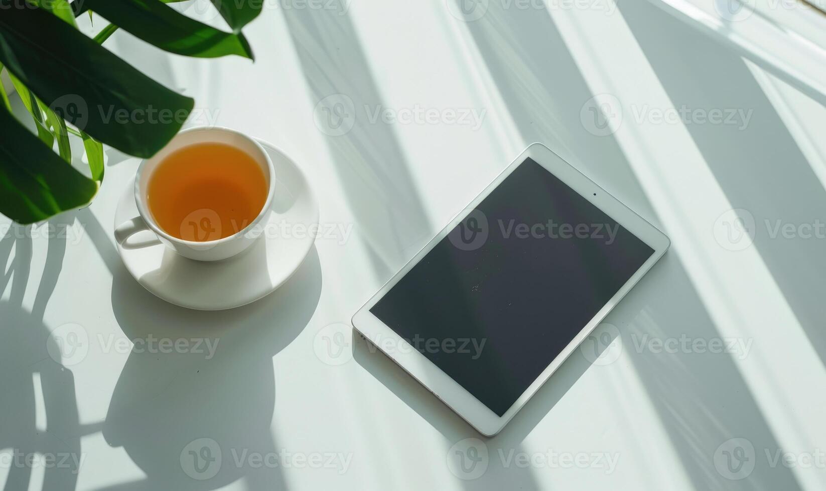 Tablet on a light gray table with a cup of tea on the left, sunlight from window photo