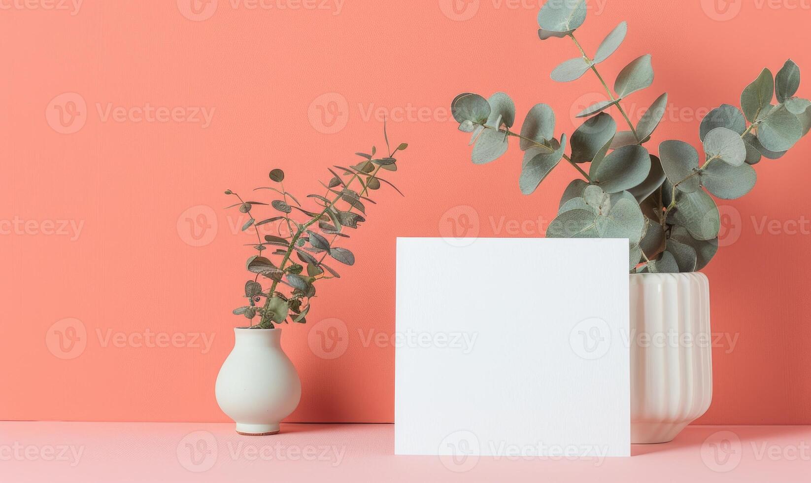 White blank card on a pastel coral table, with a small ceramic vase and a sprig of eucalyptus photo