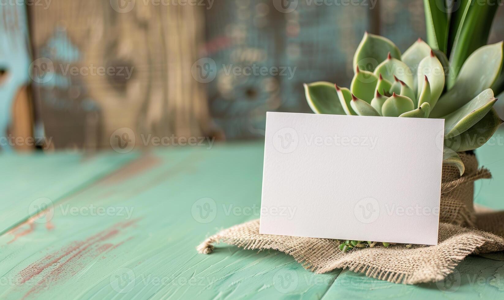 White blank card on a pastel green table, with a piece of burlap and a small succulent plant photo