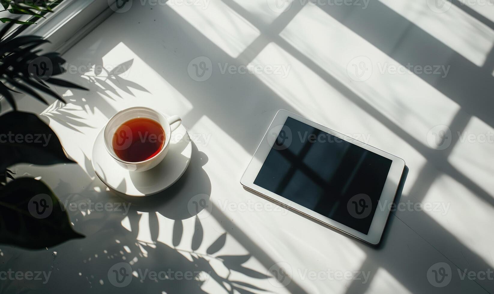 Tablet on a light gray table with a cup of tea on the left, sunlight from window photo