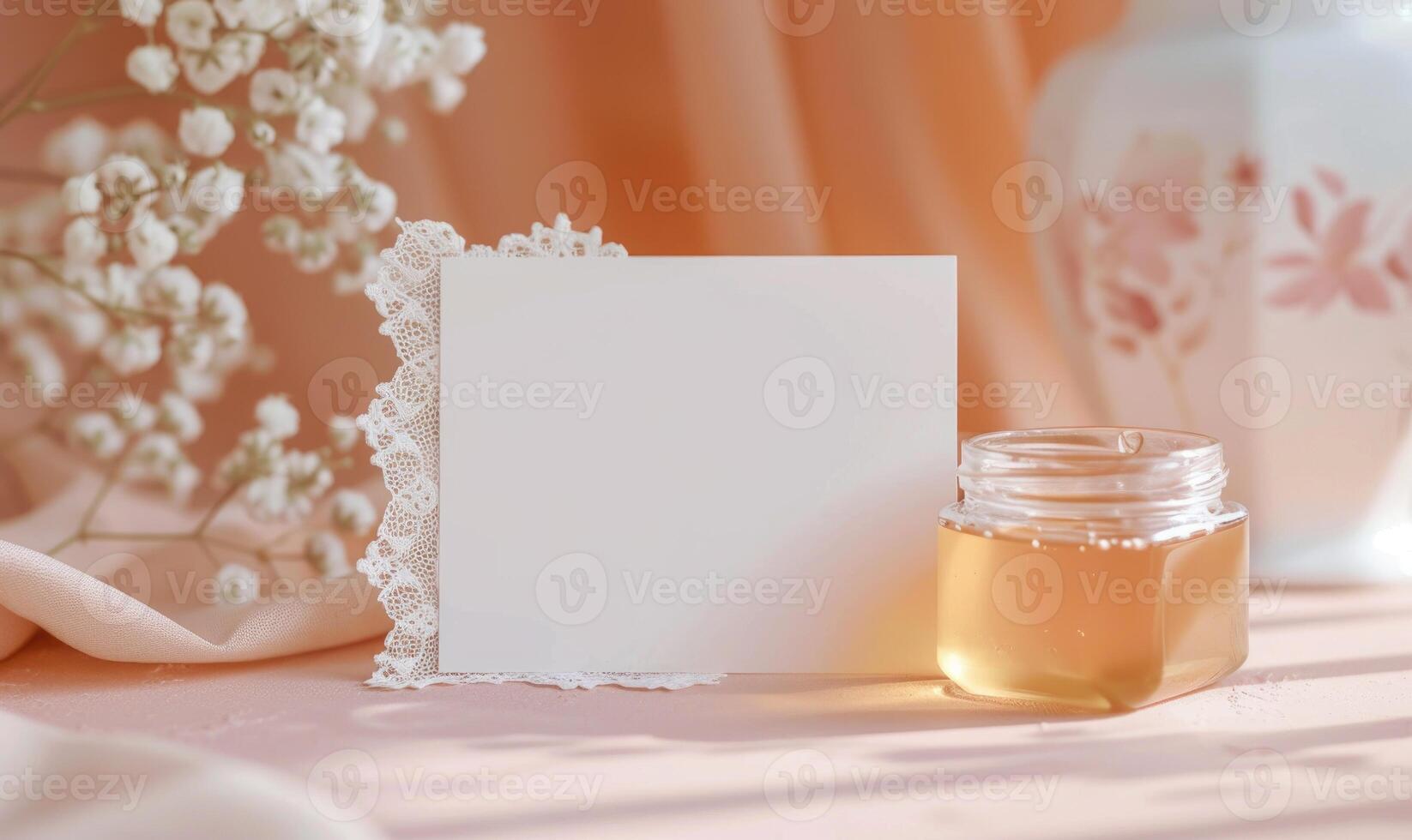 White blank card on a pastel peach table, with a delicate lace doily and a small glass jar of honey photo