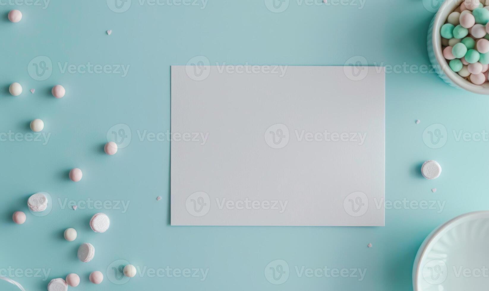 White blank card on a pastel sky blue table, with a white ceramic bowl and pastel colored beads photo