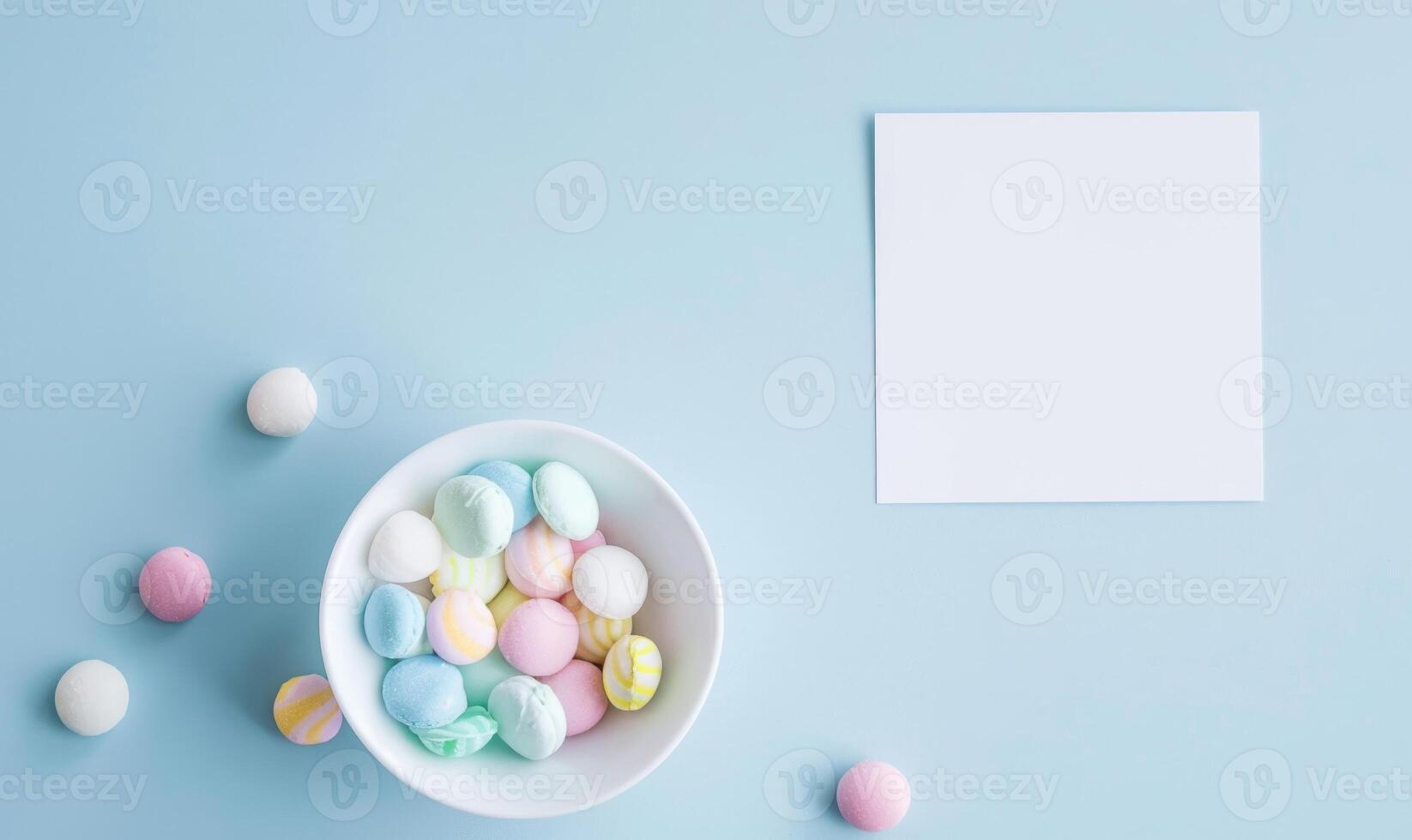 White blank card on a pastel sky blue background, with a small bowl of pastel colored candies photo