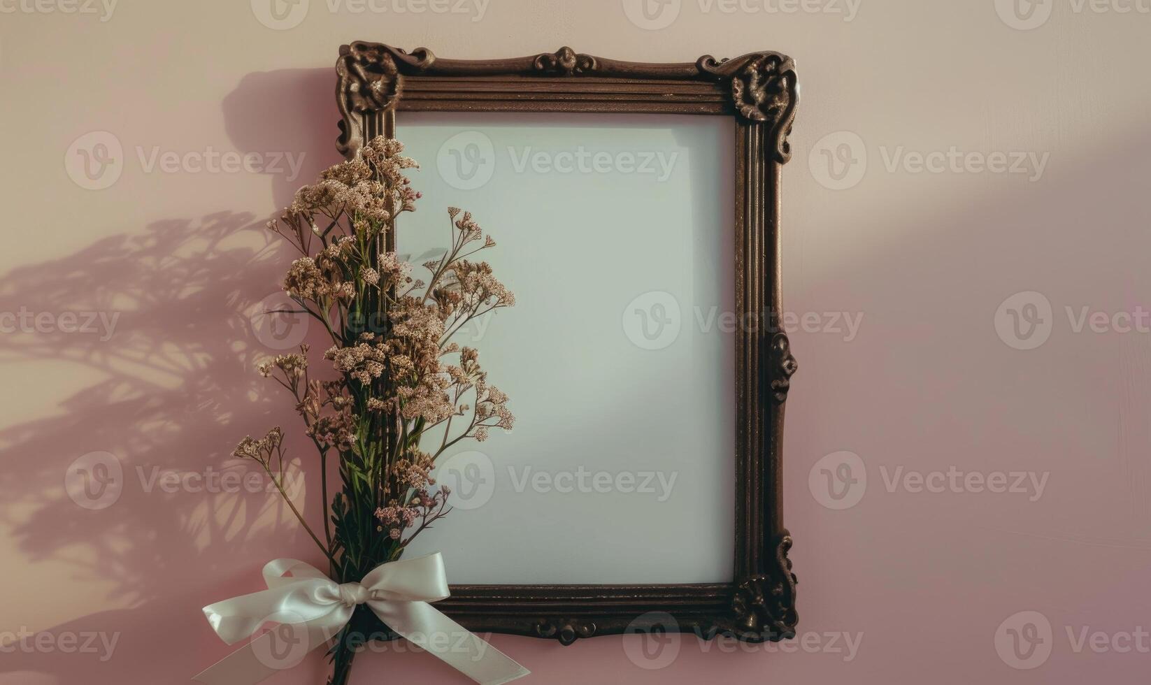 White blank card in a vintage bronze frame on a pastel lilac background, with a small bunch of wildflowers and a ribbon photo