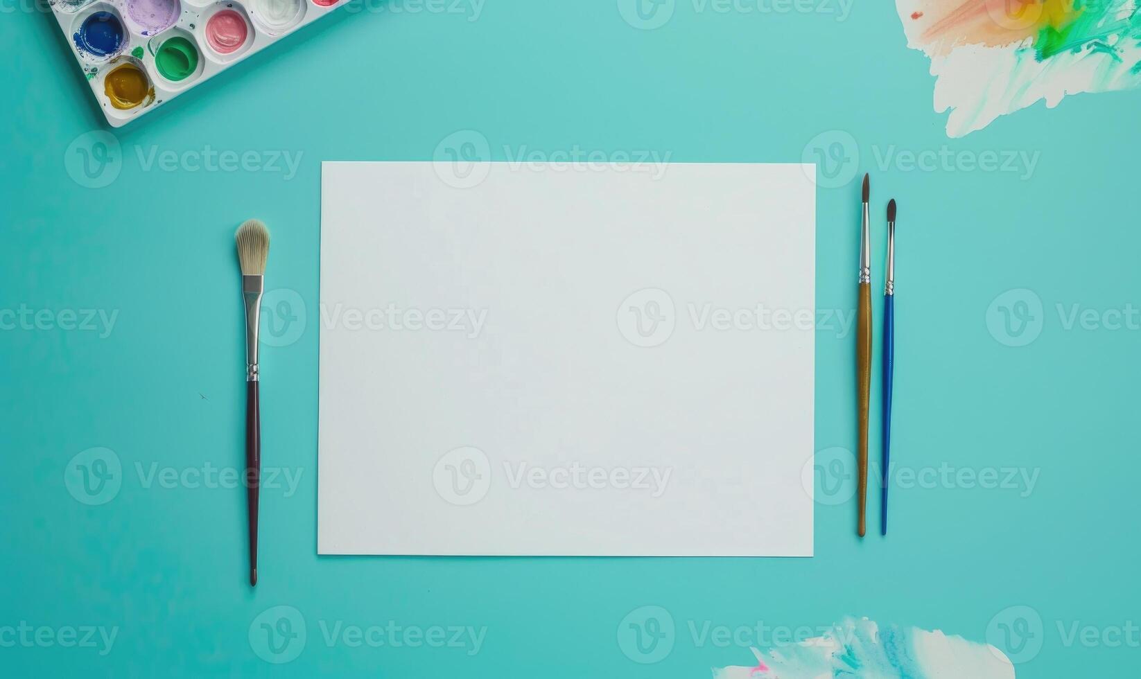 White blank card on a pastel turquoise background, with a small watercolor palette and brushes photo
