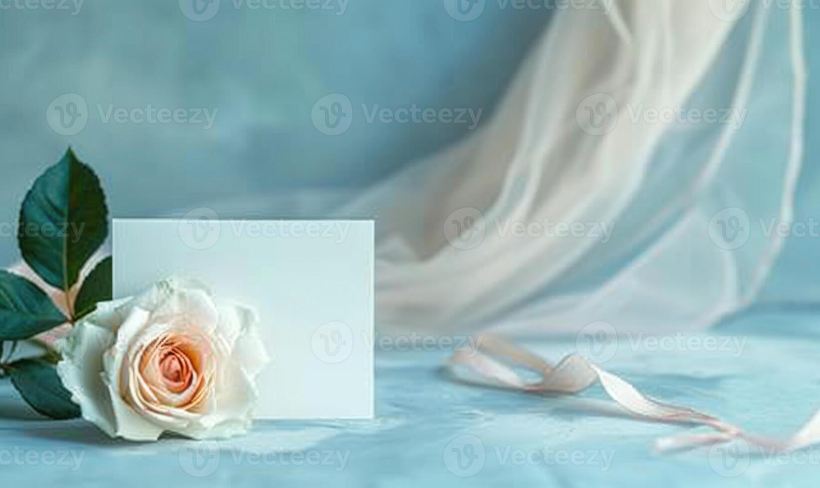 White blank card on a pastel sky blue table, with a single rose and a sheer ribbon photo