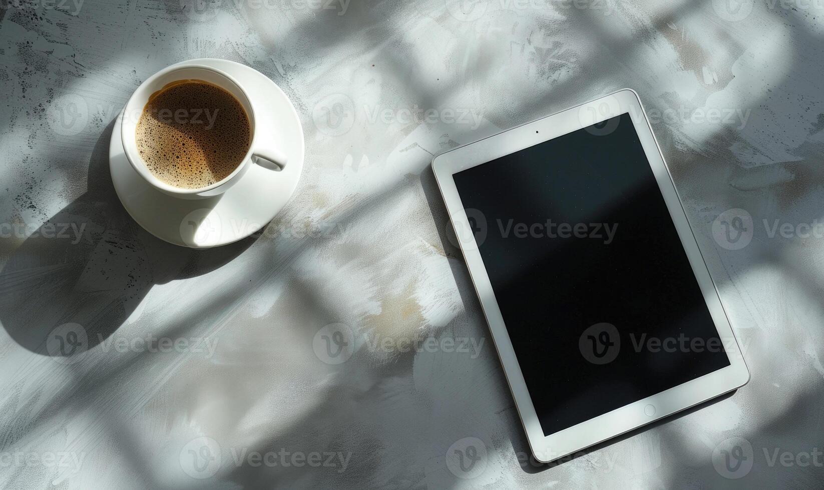 Tablet on a light blue table with a cup of tea on the right, shadow from window, top view photo