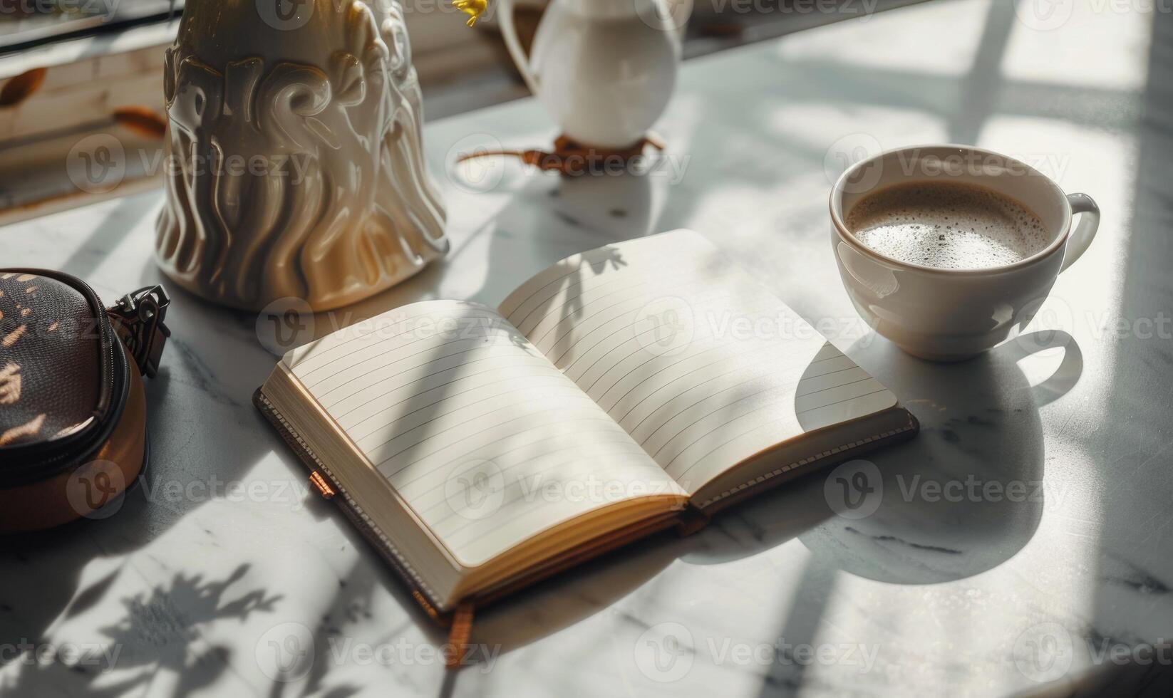 Closed notebook on a light gray table with a cup of coffee on the right and a handbag on the left photo
