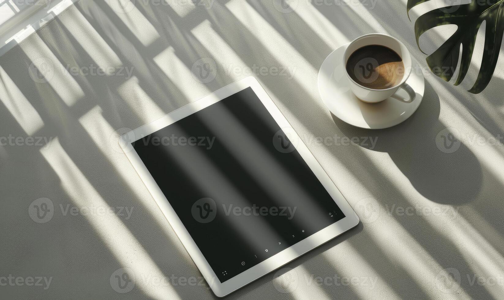 Tablet on a light blue table with a cup of tea on the right, shadow from window, top view photo