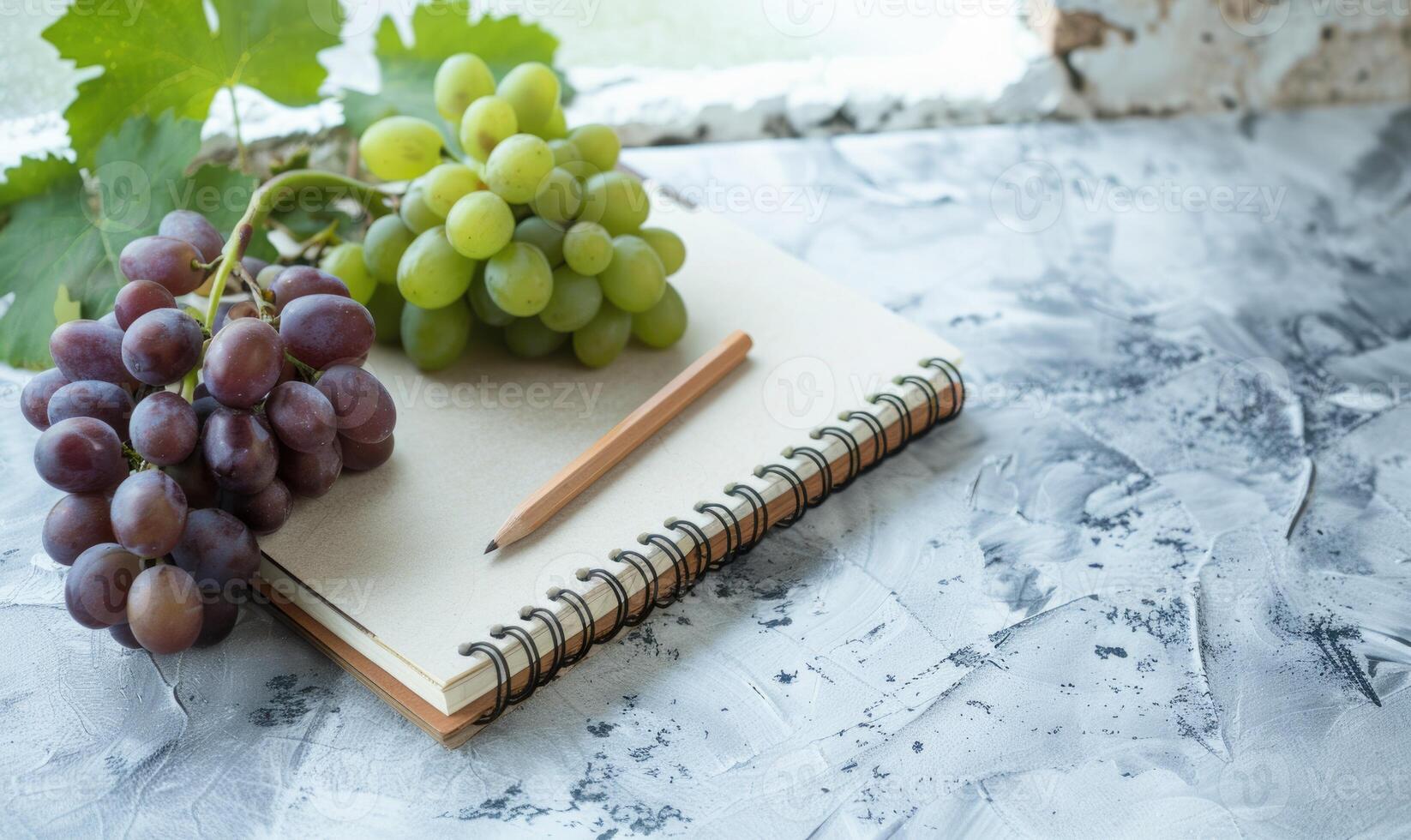 Closed notebook on a light gray table with a bunch of grapes photo