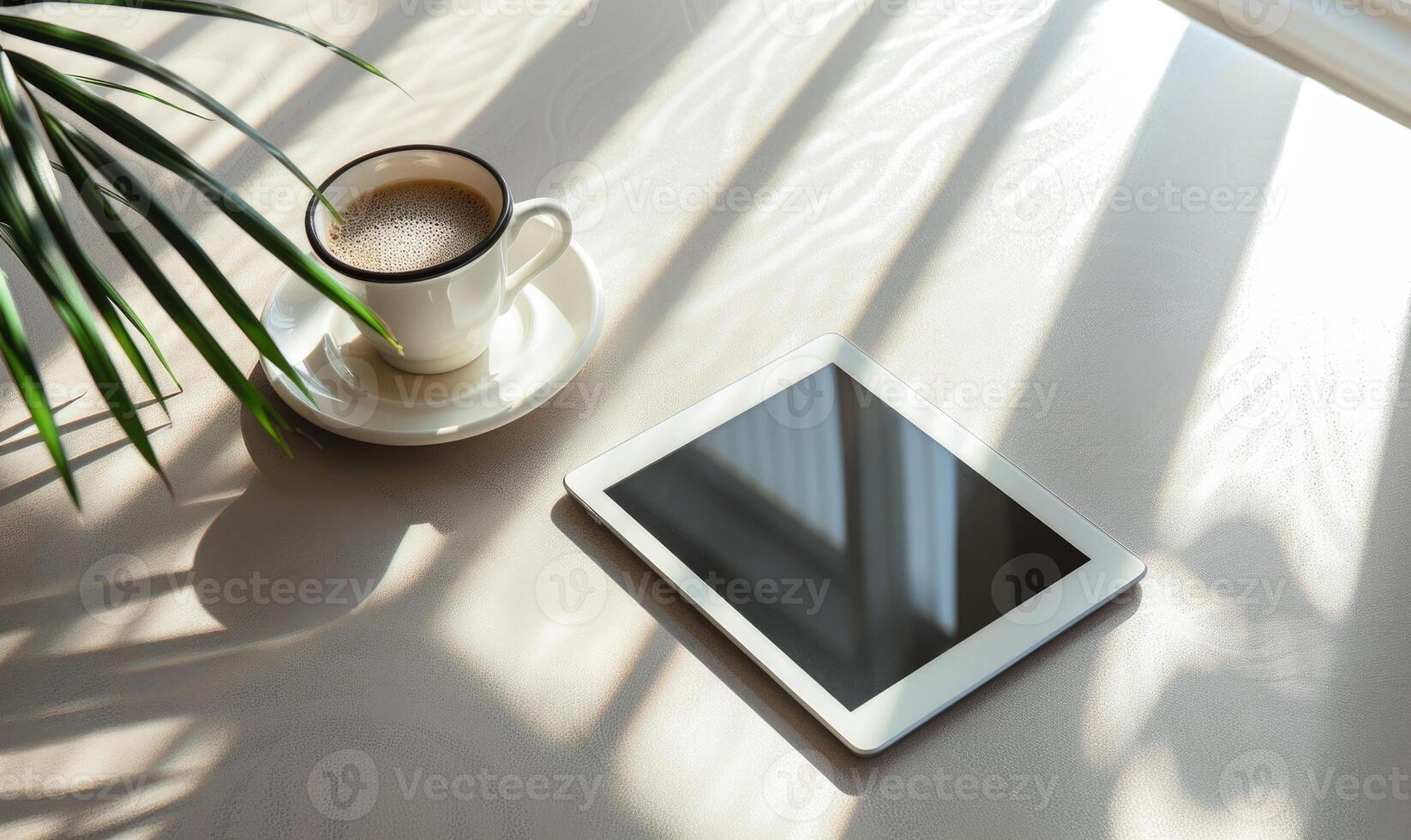 Tablet on a light blue table with a cup of tea on the right, shadow from window, top view photo