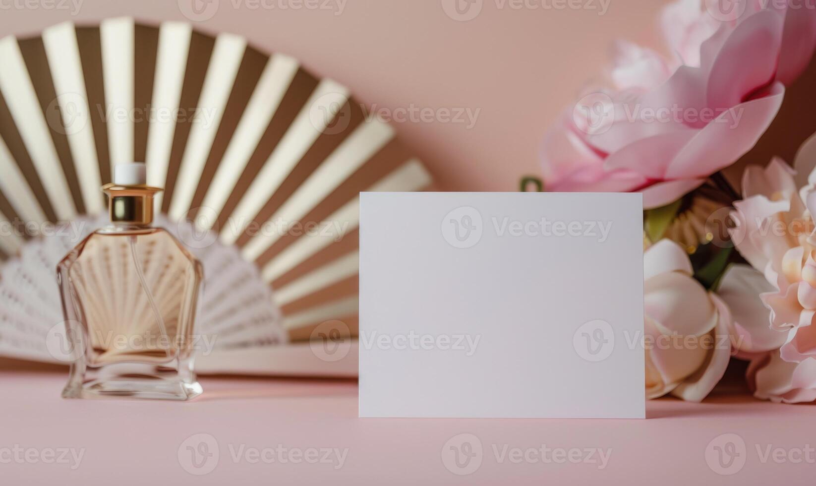 White blank card on a pastel pink table, with a delicate hand fan and a small perfume bottle photo