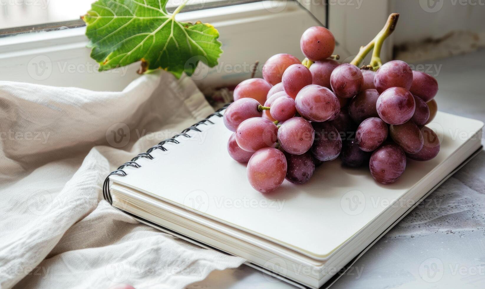 Closed notebook on a light gray table with a bunch of grapes photo