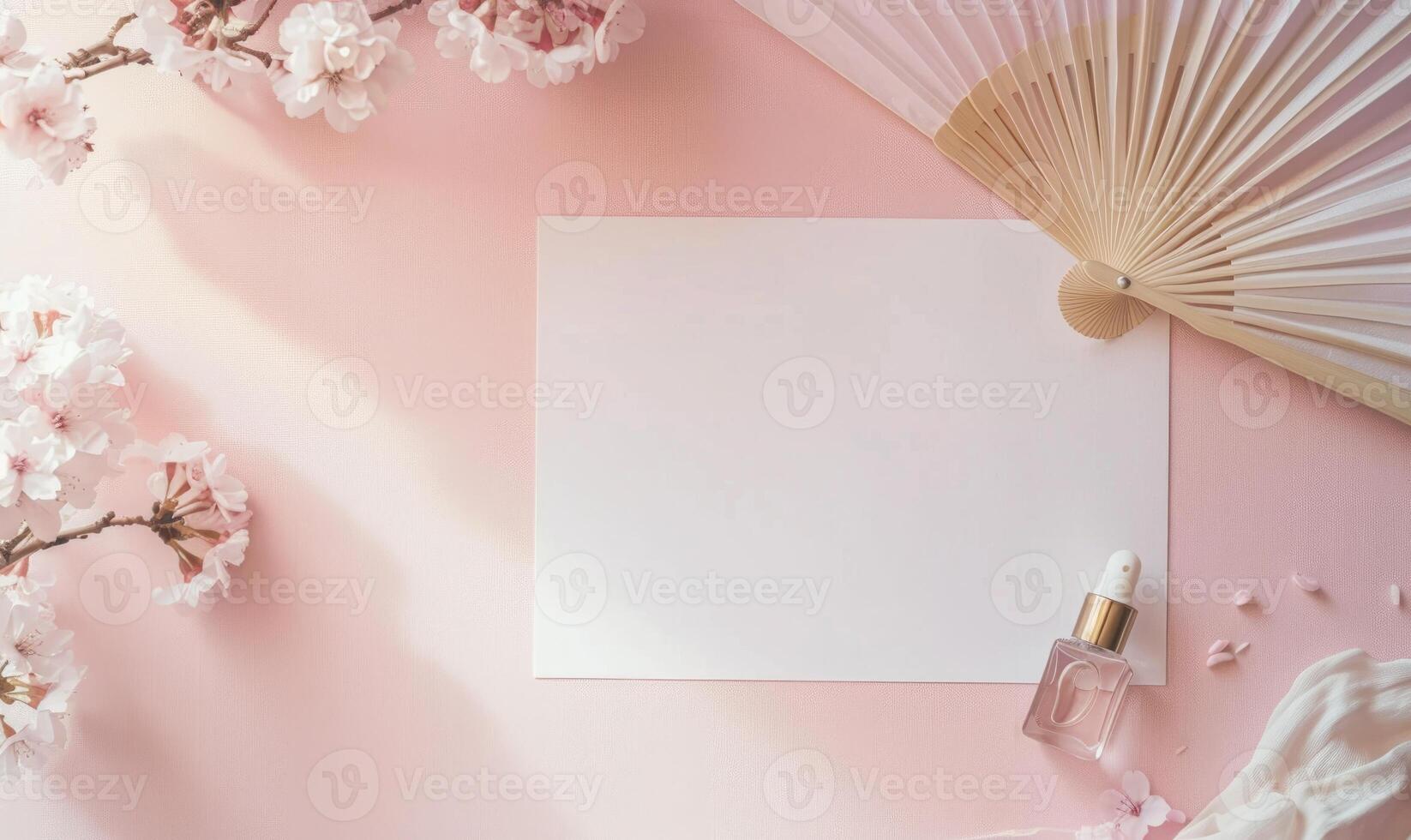 White blank card on a pastel pink table, with a delicate hand fan and a small perfume bottle photo
