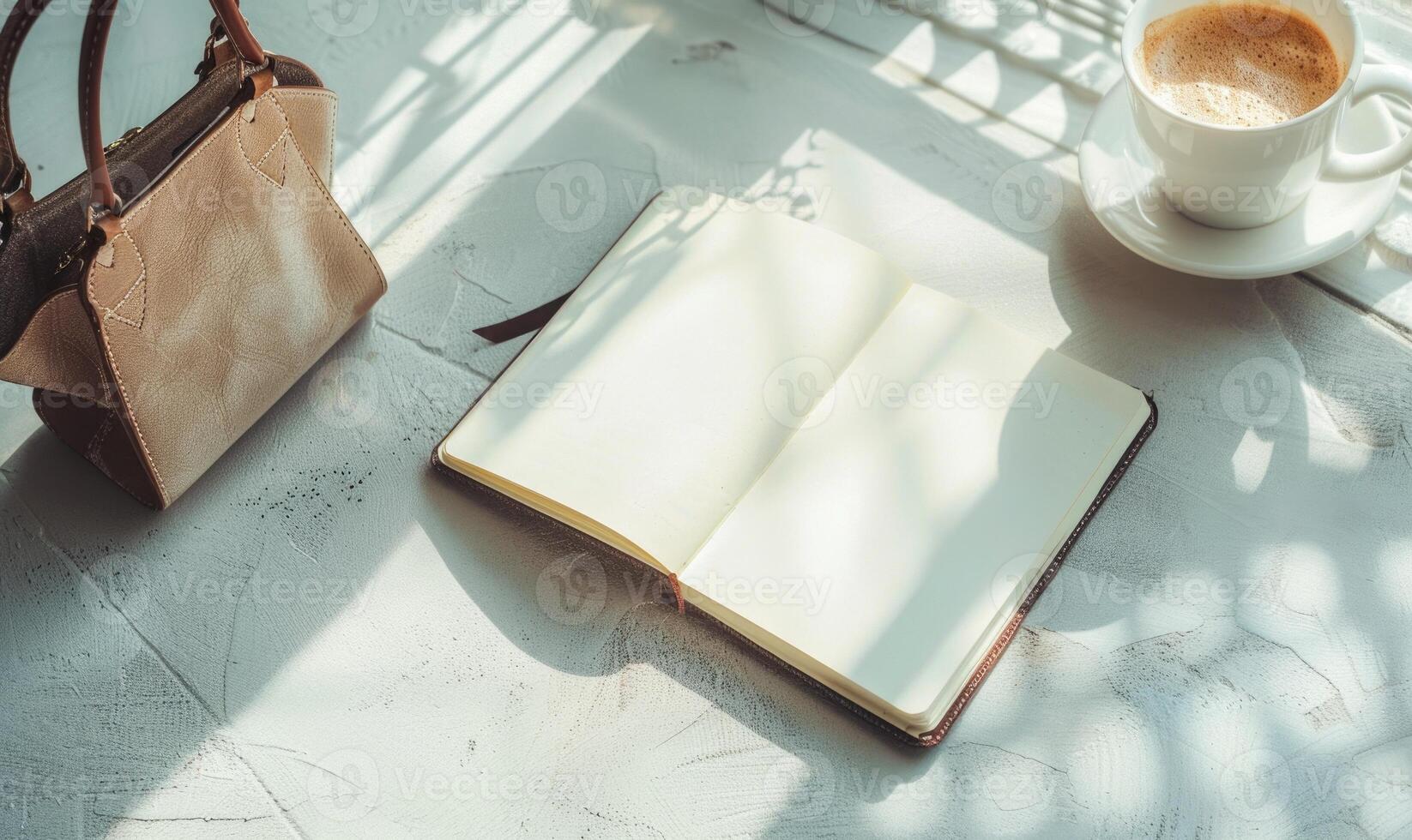 Closed notebook on a light gray table with a cup of coffee on the right and a handbag on the left photo