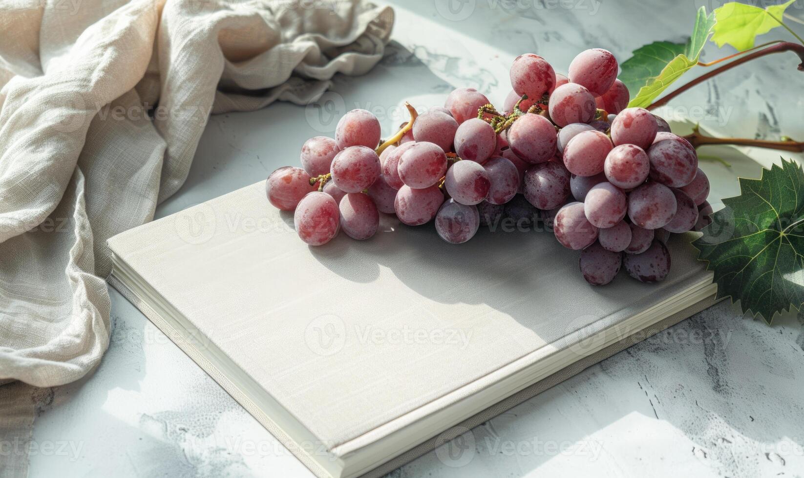 Closed notebook on a light gray table with a bunch of grapes on the right, soft window light photo