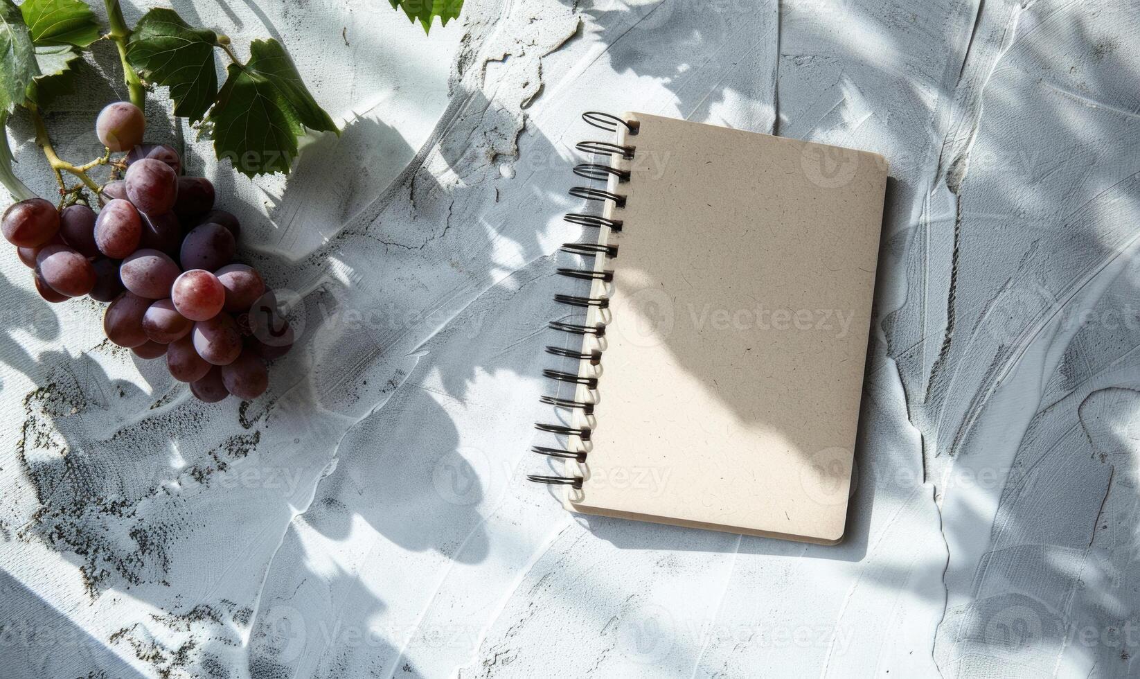 Closed notebook on a light gray table with a bunch of grapes photo