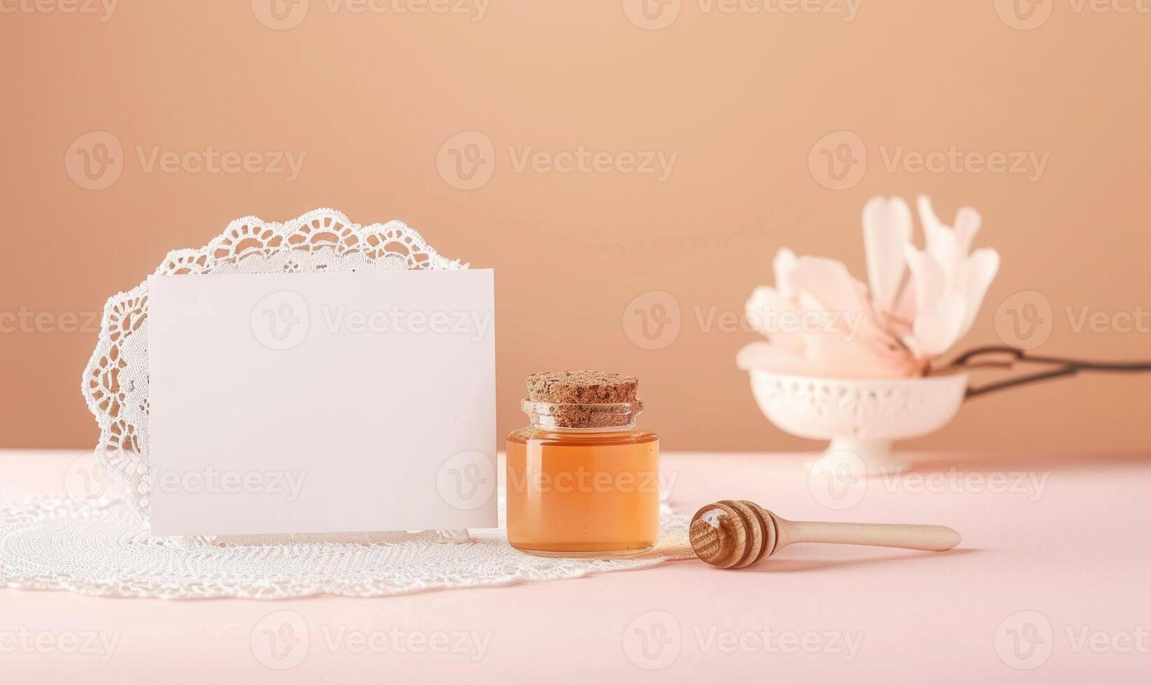 White blank card on a pastel peach table, with a delicate lace doily and a small glass jar of honey photo